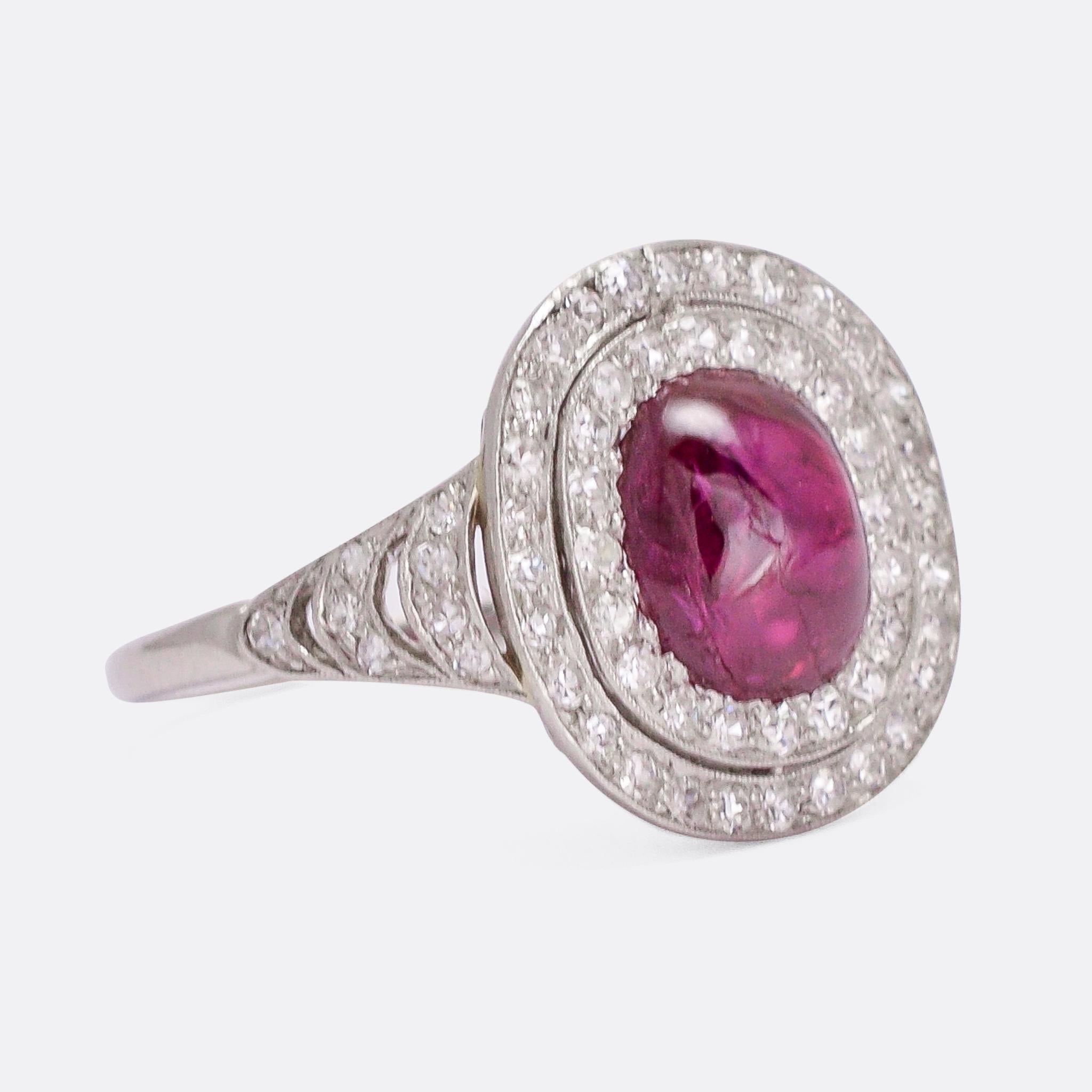 A superb 1920s cluster ring set with a principal Burma Ruby, within a double halo of white diamonds. The main stone is cut en cabochon, with an estimated weight of 3.1 carats. The settings are finished in fine millegrain detailing, and the shoulders