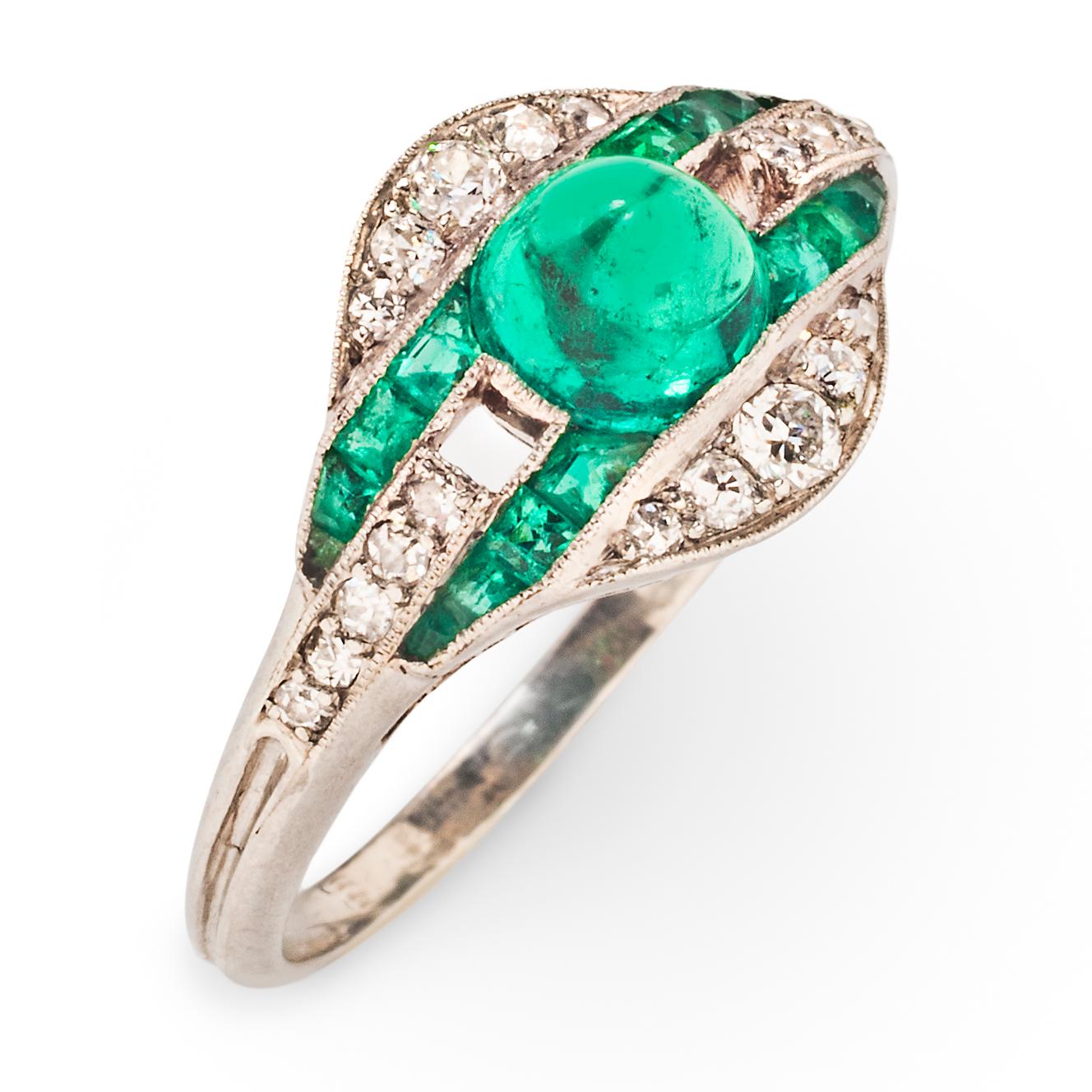 This delicate Art Deco ring features a vibrant Columbian cabochon emerald in a platinum openwork mount set with diamonds and emeralds.  The central stone is positioned between two parallel lines of calibre-cut channel set emeralds separated by