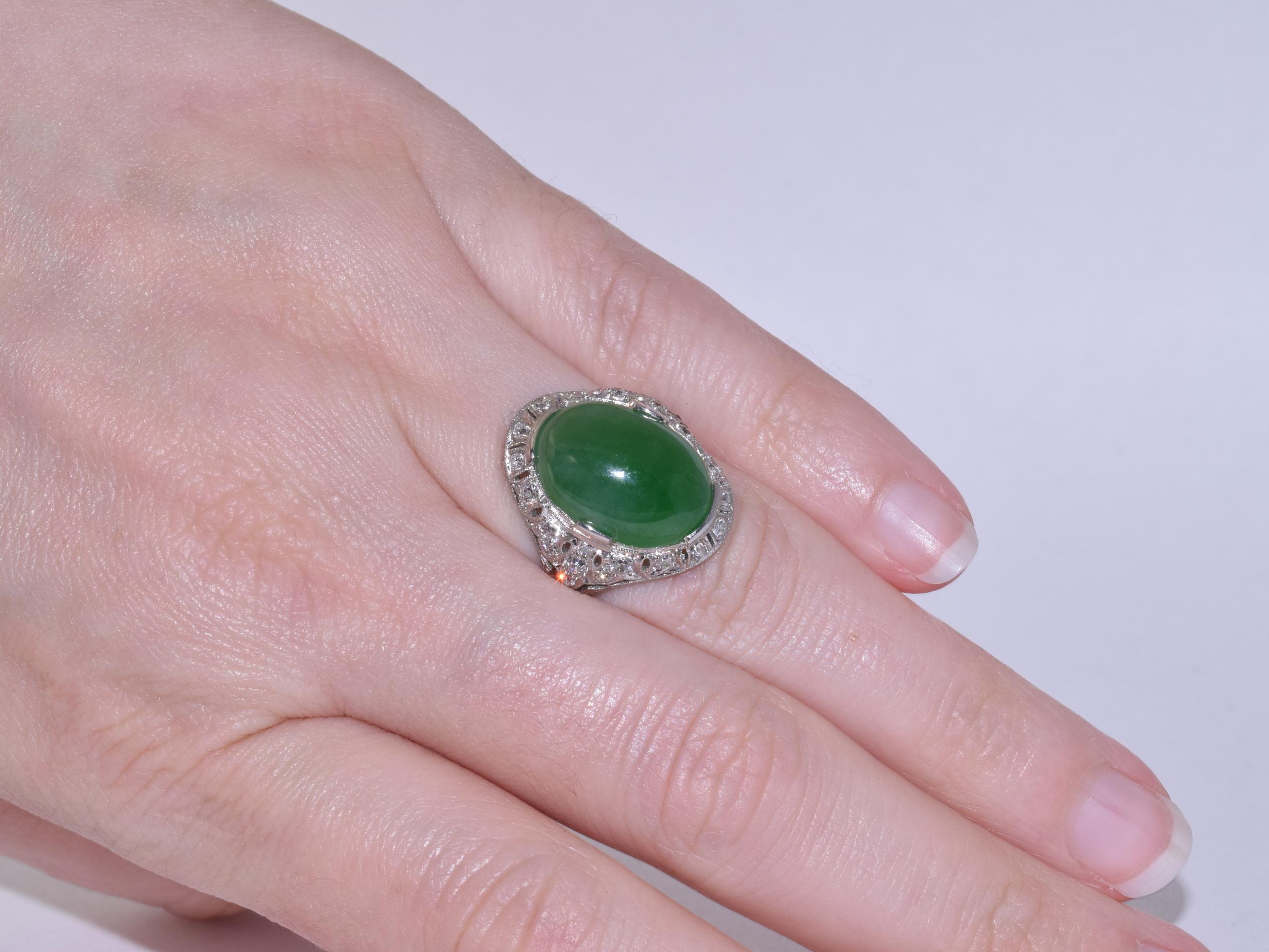A brightly colored oval jadeite cabochon is accented with old European cut diamonds totaling approximately 0.55 carats set in a delicately pierced platinum ring with millegraining and hand-engraved details. Ring size 6.25. The jadeite cabochon