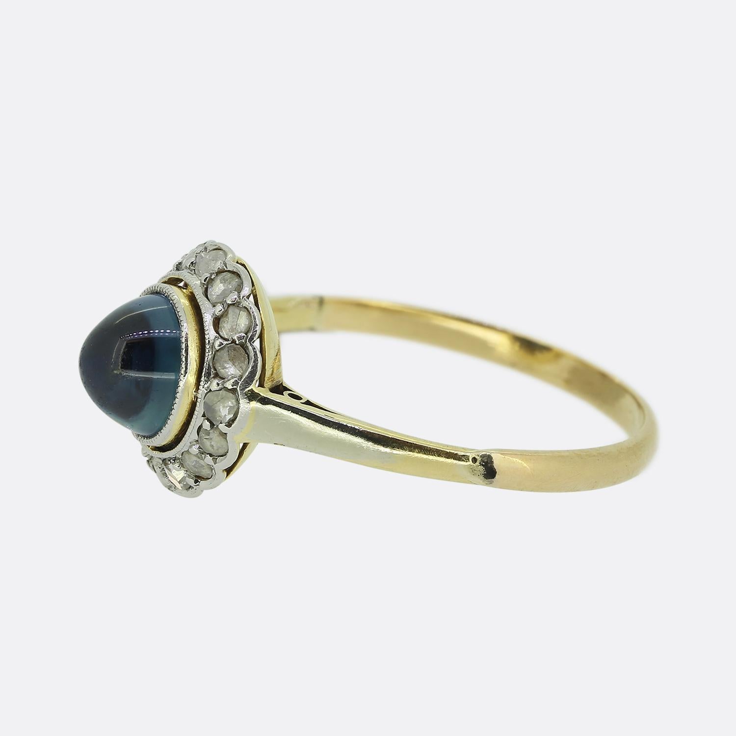 Here we have a lovely sapphire and diamond cluster ring crafted during the early stages of the Art Deco movement. A bold blue iridescent cabochon sapphire sits proud at the centre of the face and is contained within a fine milgrain detailing. This