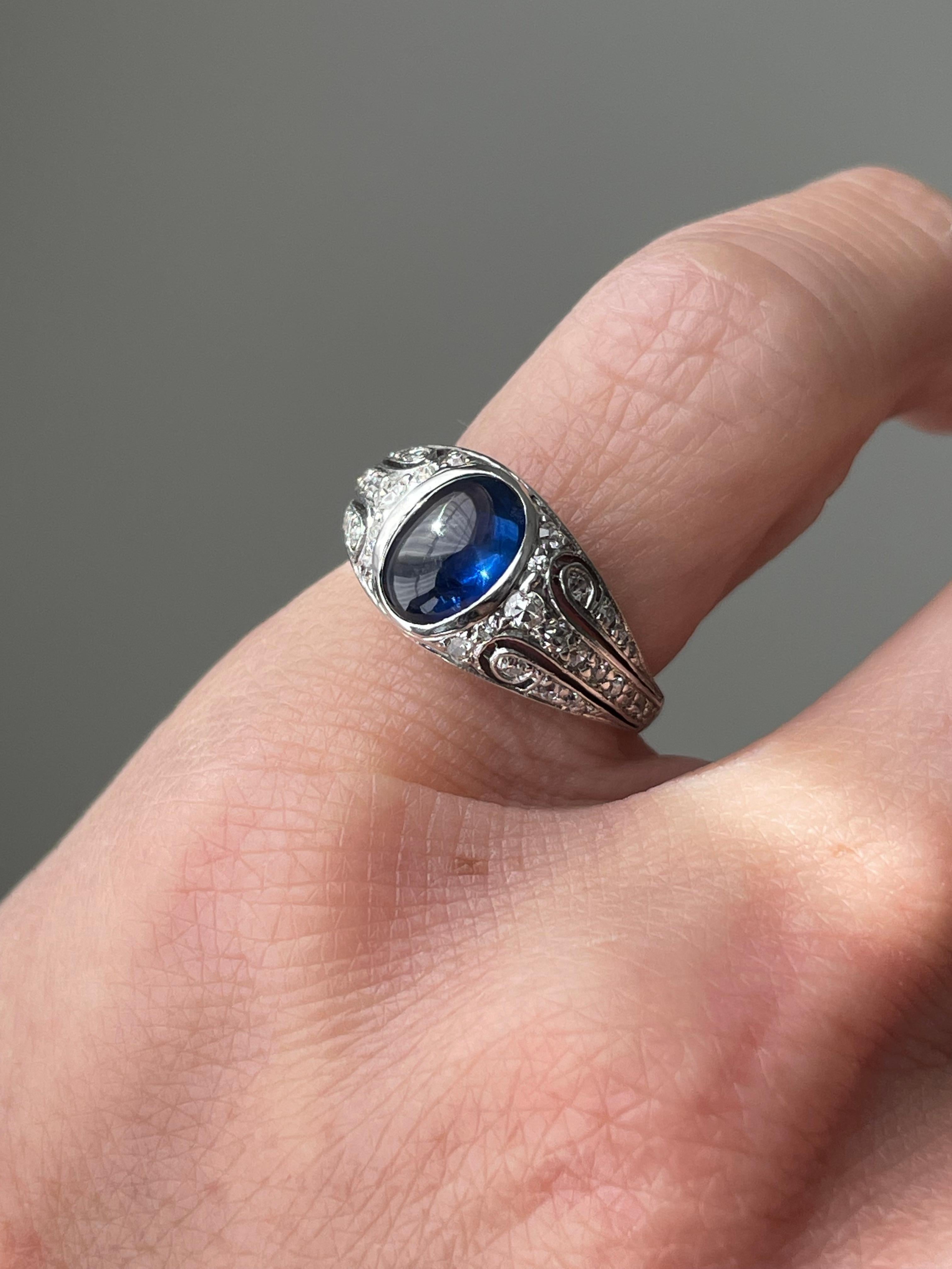 Intricately hand pierced scrolls lined with shimmering single-cut diamonds frame a glowing 1.8 carat sapphire cabochon in this delightful Art Deco ring. Hand fabricated in platinum, this ring is currently a size 3.25. Please note, this ring can only