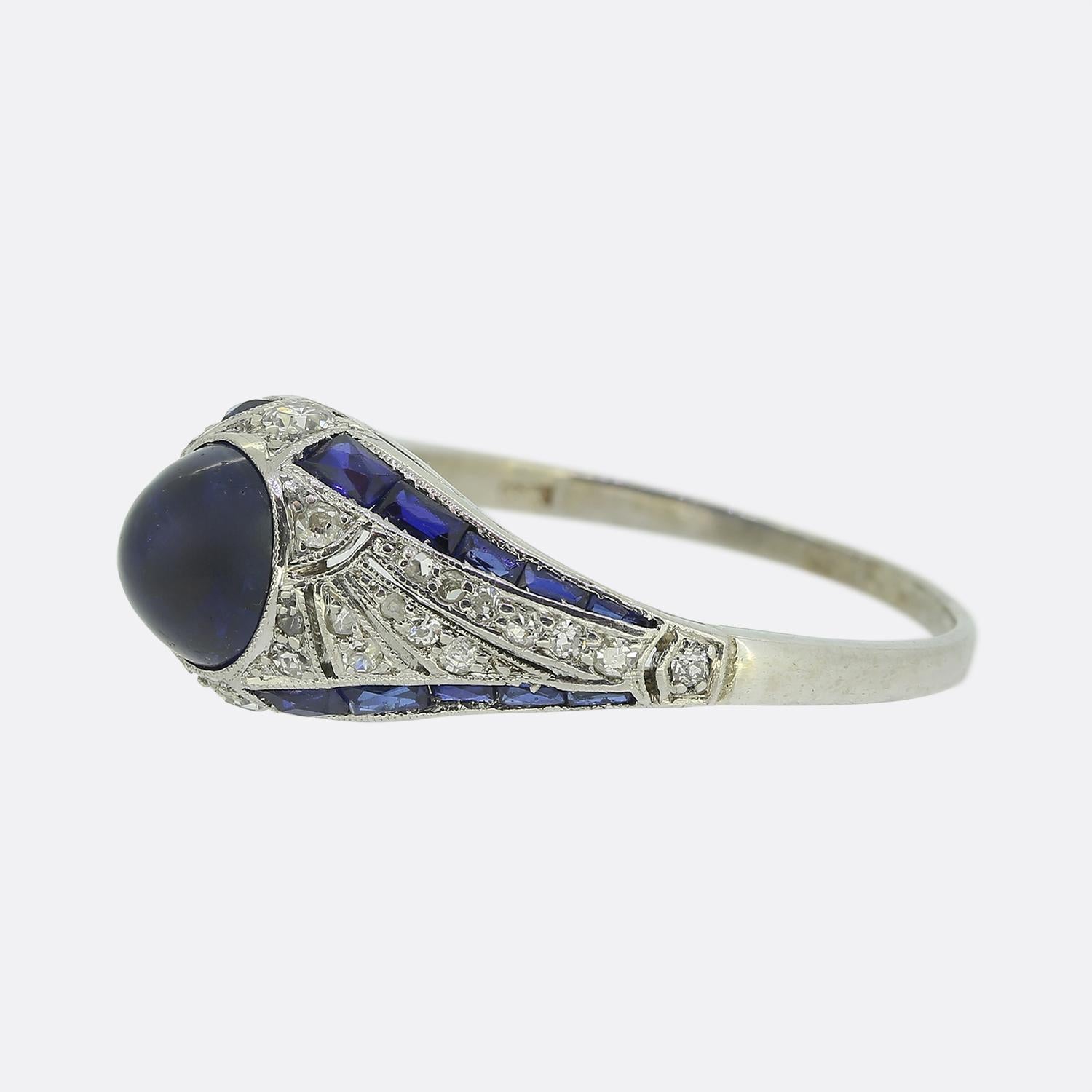 Here we have an original Art Deco sapphire and diamond ring. This platinum piece features a centralised round cabochon sapphire possessing a deep navy blue colour tone. This principal stone is surrounded by a series of old European and rose cut