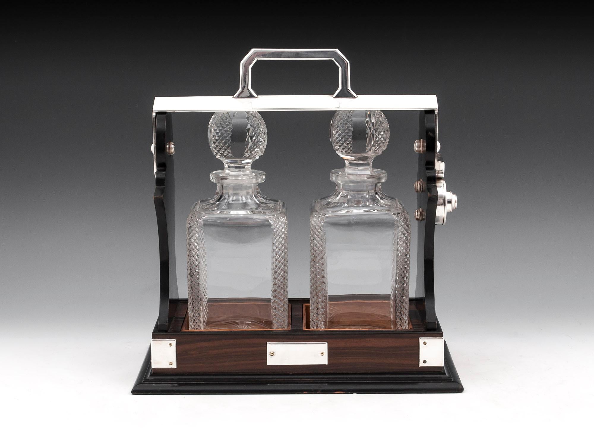 Art Deco calamander tantalus with simple square silver plated brackets around the base and vacant initial plaque. The top has a silver plated swing arm holding the two fabulous lead crystal decanters, each with chamfered corners with a diamond cut