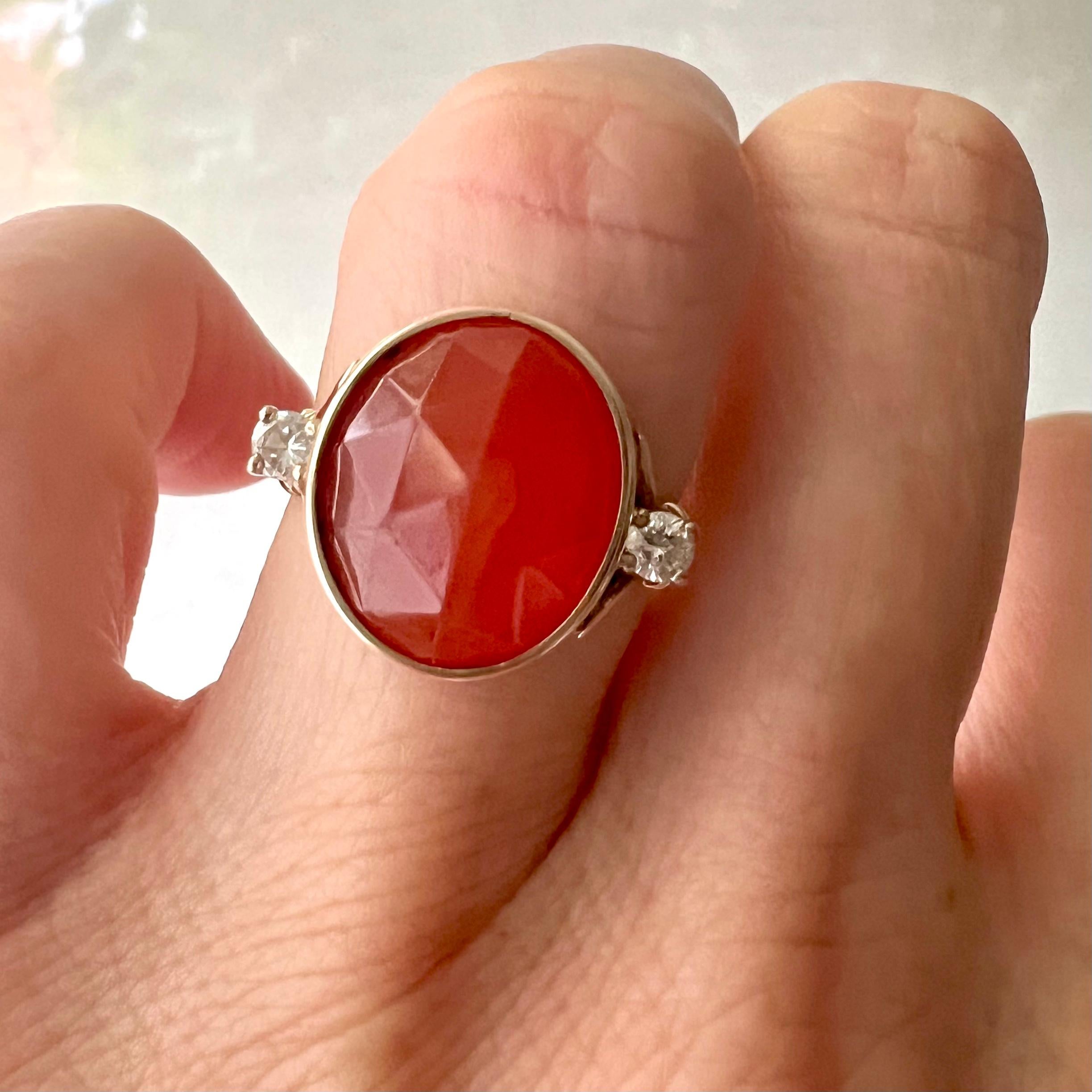 This Art Deco carnelian and diamond ring features a orangish translucent oval faceted carnelian created with a bright white brilliant cut diamond on either side of this beautiful ring. The diamonds are prong set and the shank of the ring is crafted