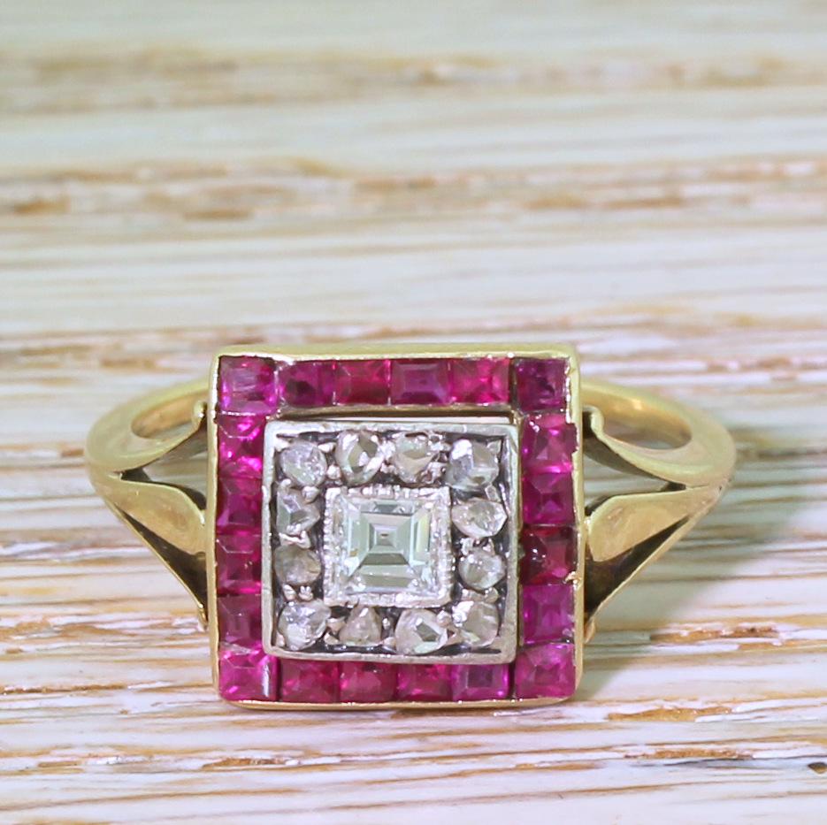 A wonderful Art Deco ruby and diamond ring. At the centre is a blindingly white carré cut diamond, rubover and milgrain set within a surround of twelve rose cut diamonds and twenty synthetic pinkish red rubies. The square cluster features a simply