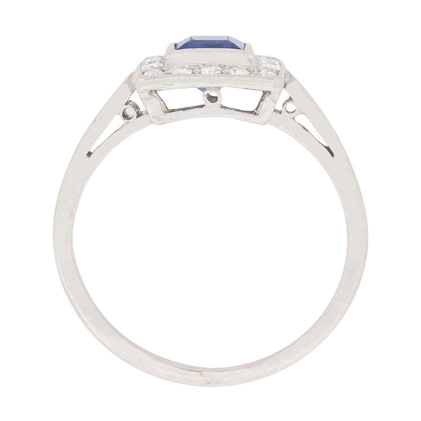 Dating back to the 1920s, this delicate ring features a carre cut sapphire in the centre. It is a wonderful blue and weighs 0.40 carat. It has ben rub over set and haloed by 16 8-cut diamonds. Each weighs 0.01 carat, bringing the total to 0.16 carat