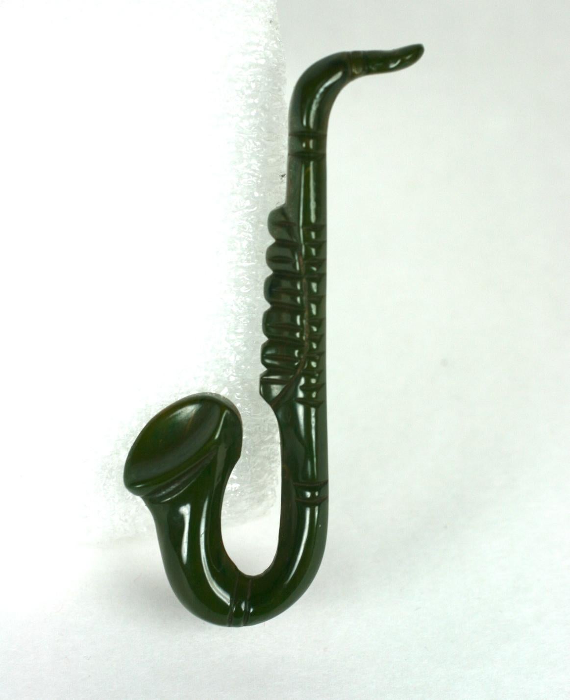 Rare Broche Saxophone Art Déco en bakélite sculptée. Sculpté à la main en bakélite marbrée verte de fin de journée avec un motif musical inhabituel.  De l'âge du jazz des années 30, aux États-Unis.
3.25