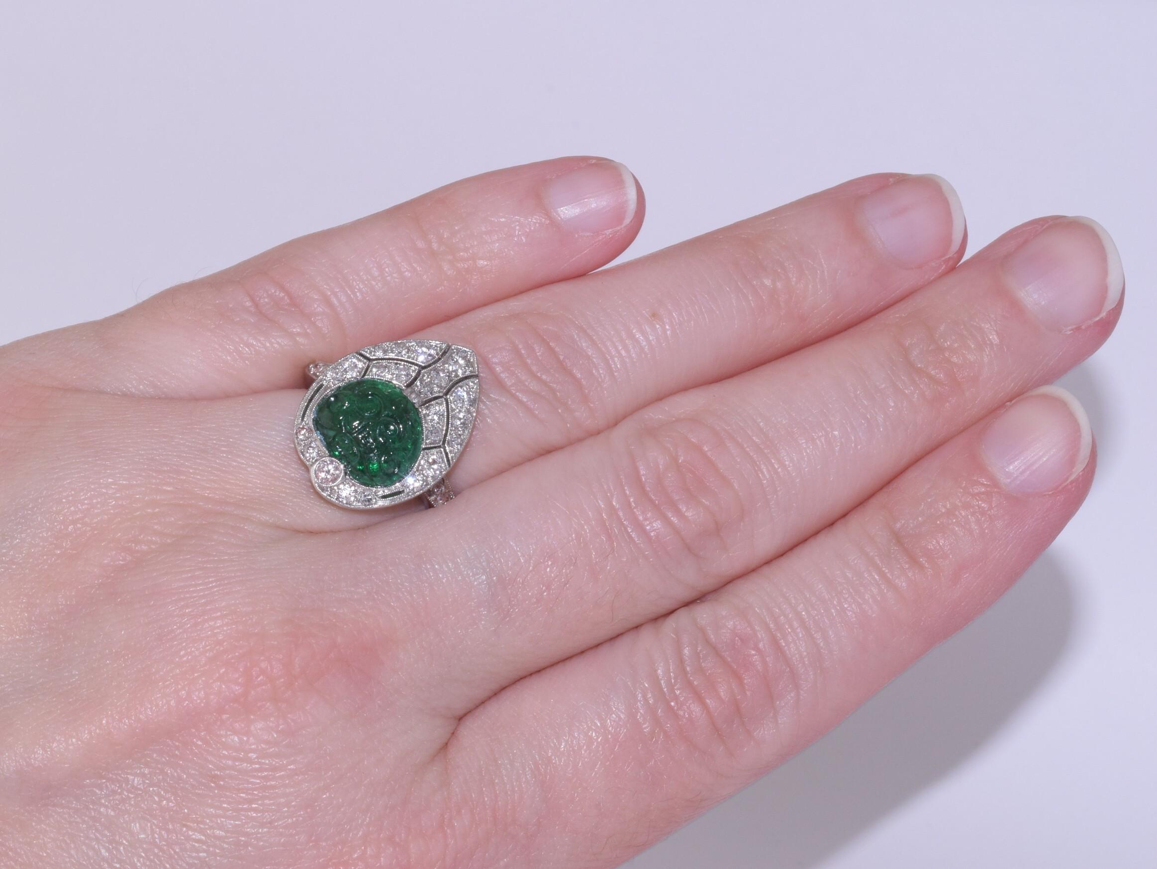 A floral motif carved emerald weighing approximately 1.40 carats is set in a stylized palmette accented with a total of approximately 0.80 carat of round and single cut diamonds in a platinum mounting. Circa 1920s.       

Top element of ring