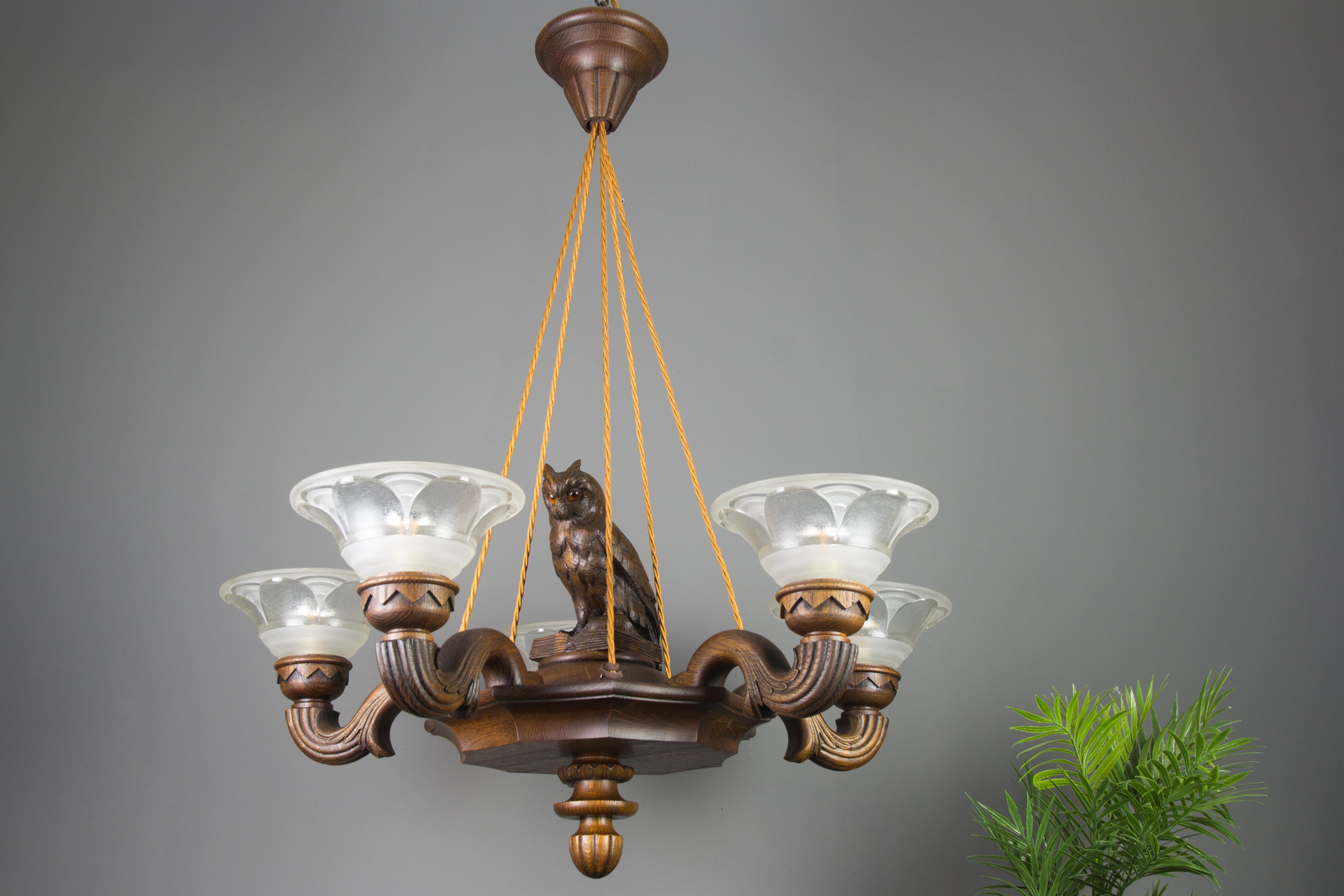 Beautifully carved wooden chandelier with five arms, each with a wonderfully shaped glass lampshade made and marked by Ezan, France. This large antique chandelier features an adorable owl figure sitting on an open book in the center of the