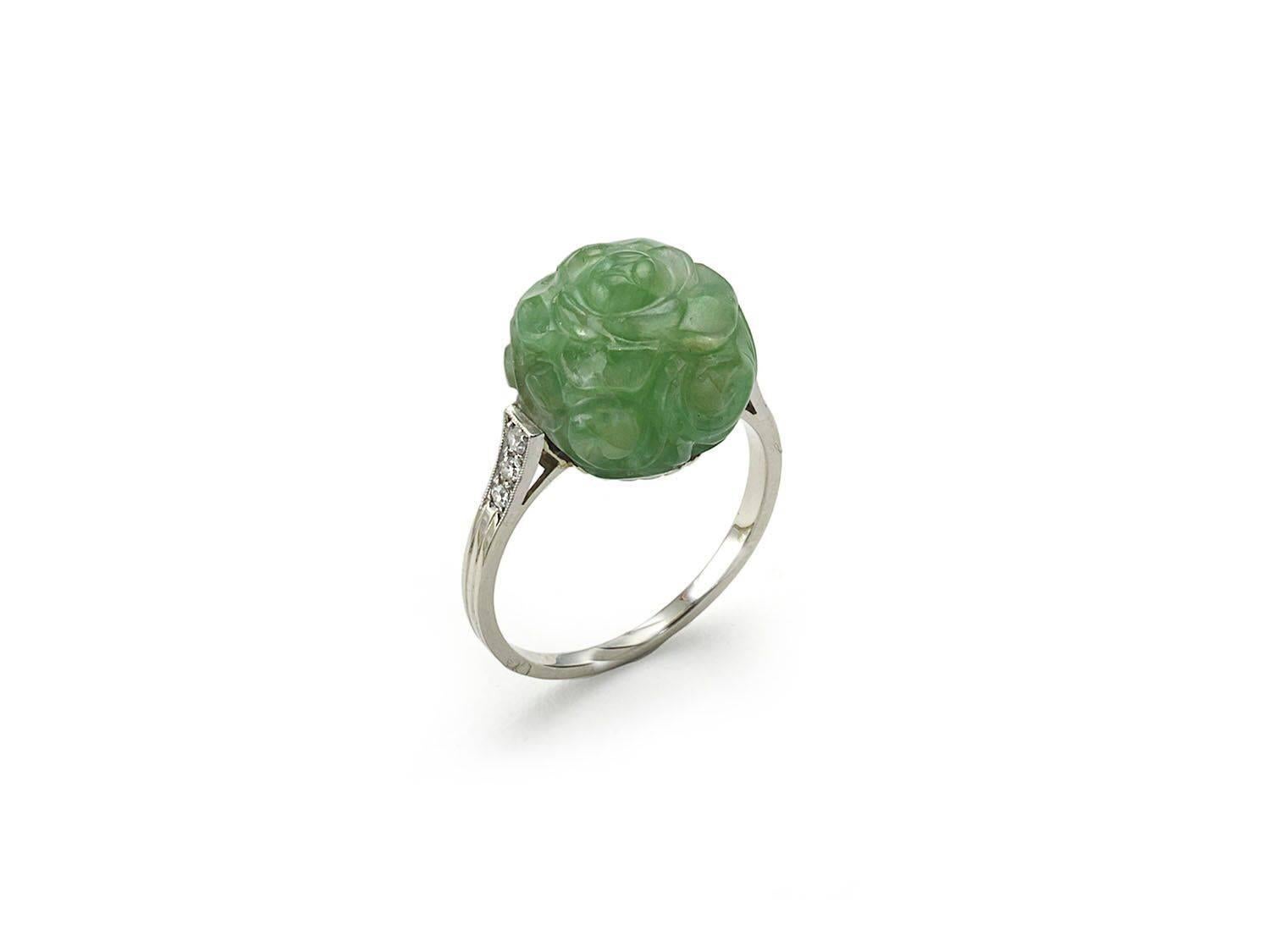 A carved jadeite jade ring, in the form of a rose, with eight-cut diamonds in the shoulders, in platinum millegrain edged settings, mounted in 18ct white gold, with a French dog mark, for the 18ct white gold mount and an eagle mark for the platinum