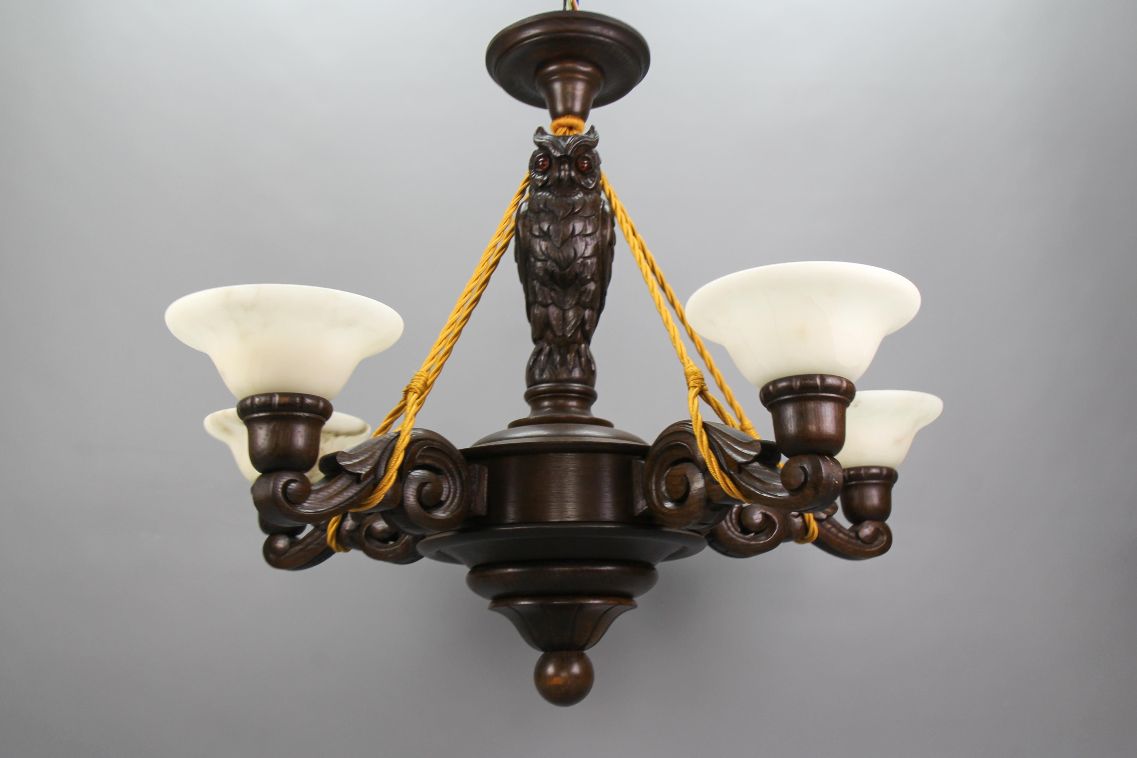 Beautiful and impressive five-light oakwood chandelier with an owl figure, Germany, the 1930s. This hand-carved chandelier features five arms, each with a white alabaster lampshade, hung on five ropes/wires and connected to a wooden ceiling canopy.