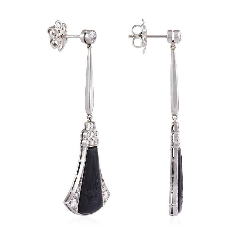 A pair of Art Deco diamond earrings with fan-shaped pendants set with carved onyx plaques depicting urns, in platinum.