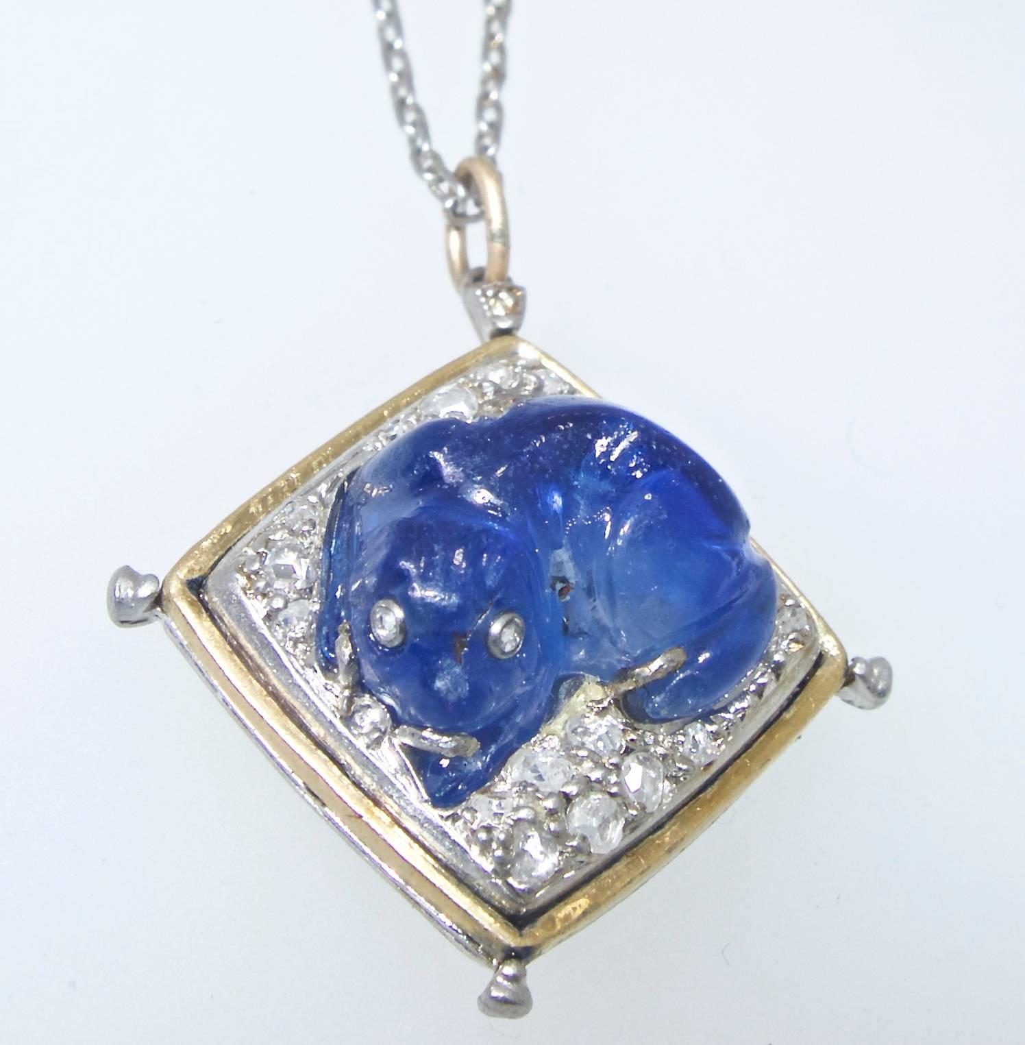 Antique 3.5 ct natural untreated, bright blue Ceylonsapphire carved in the shape of a dog lying on a bed of rose-cut diamonds in the center of the 18K and platinum pendant which is slightly less than one inch in diameter.  This doggy has a collet