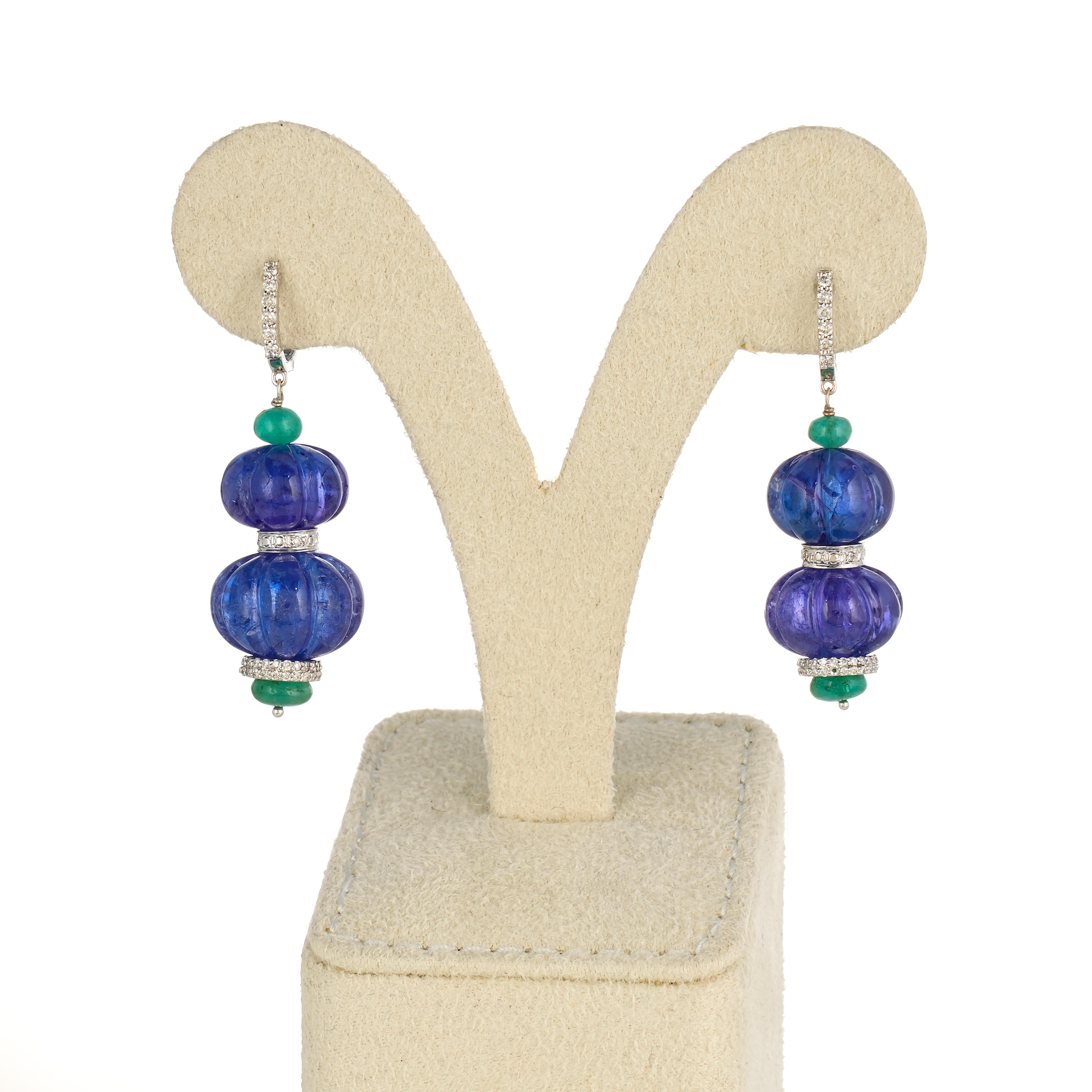 A pair of art-deco inspired carved 82.82 carat Tanzanite and 4.05 carat Emerald beads dangle earrings, with lever back diamond studded hangings. The earrings are around 2 inches long, and are set in 18K white gold. 

Details:
Tanzanite Carved Beads: