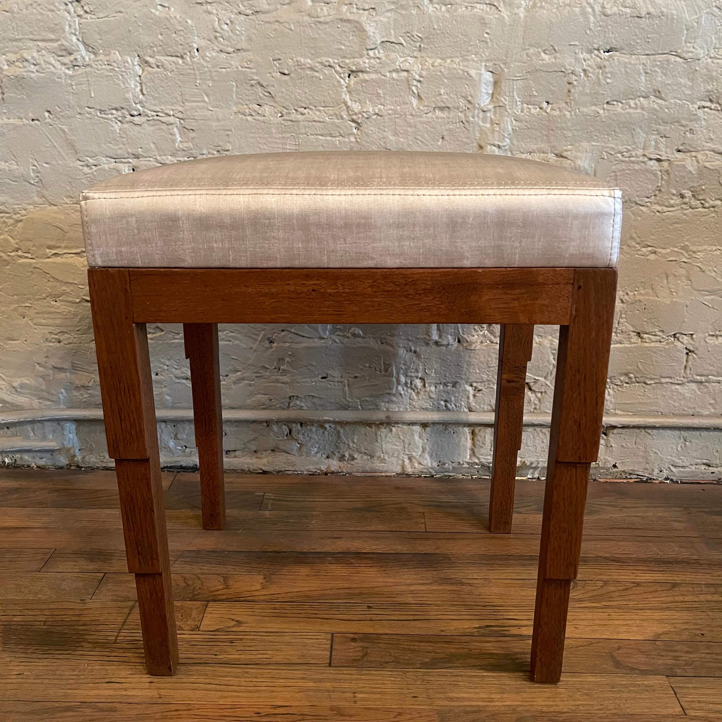 Art deco, ottoman or stool features a carved walnut base with a newly upholstered seat in light silver gray, durable, artificial silk.