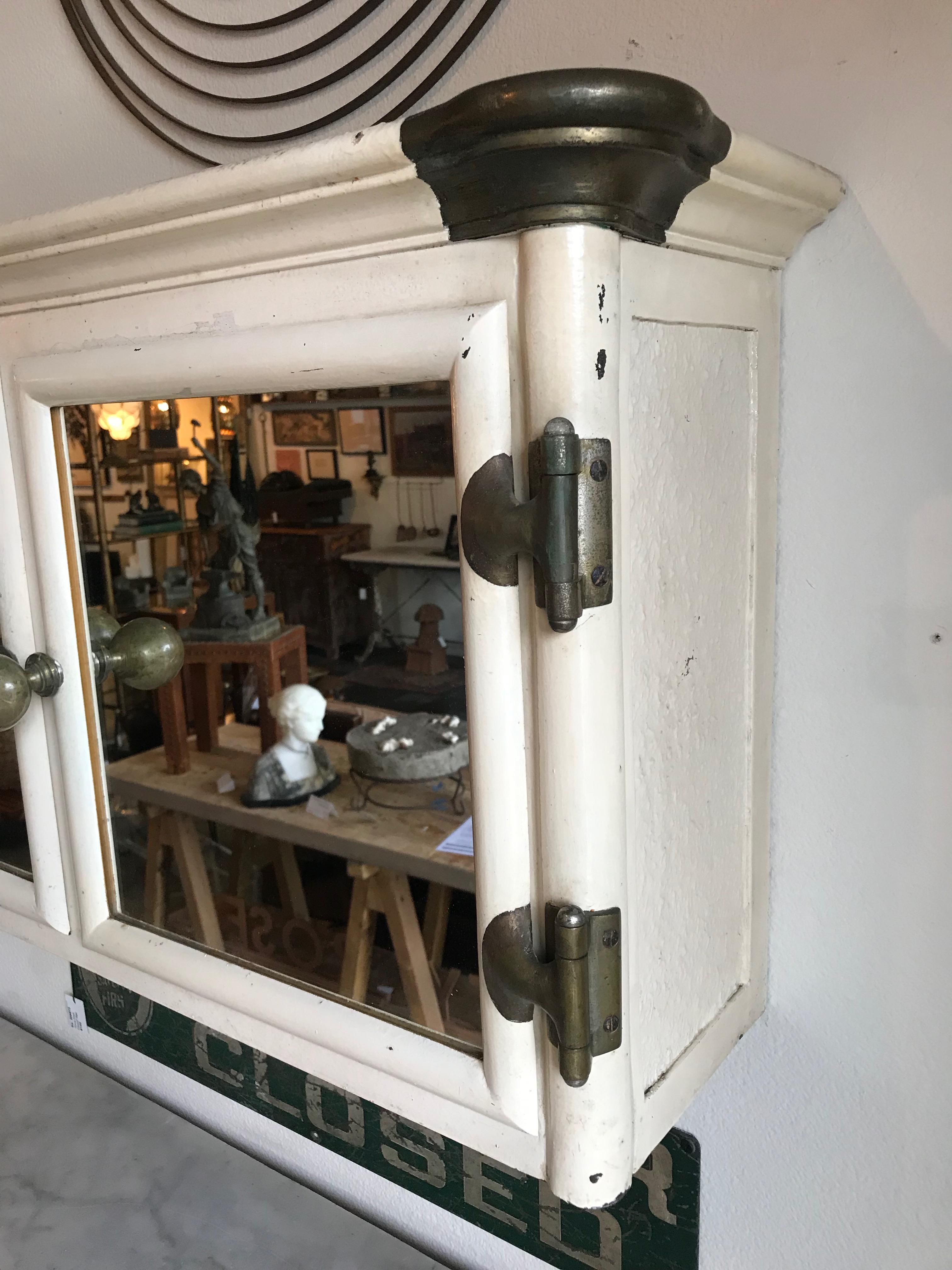 This is an Art Deco painted cast iron wall mount mirrored medicine cabinet from England. Oversized brass knobs, corner caps, and hinges make this incredibly attractive and unique. The interior is missing its shelves, however glass shelves can easily