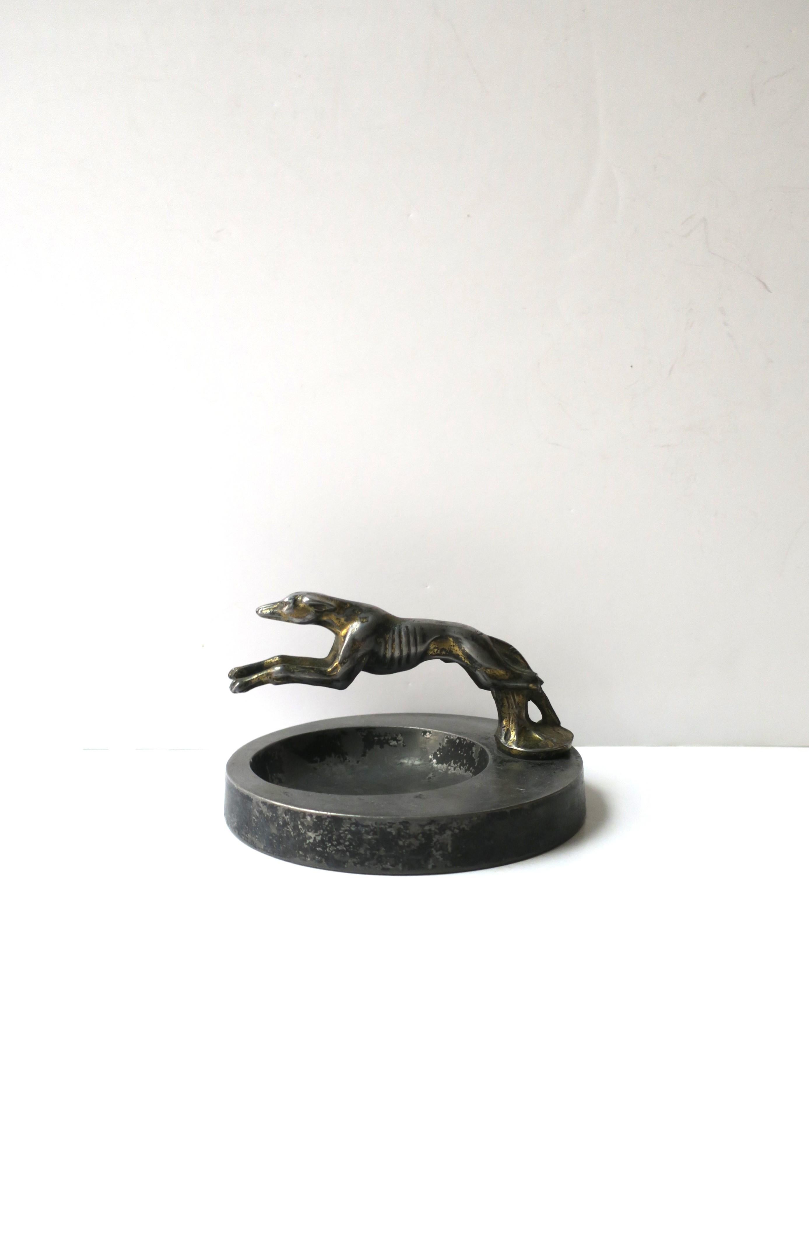 A substantial metal catchall vide-poche with greyhound whipped dog sculpture, Art Deco period, circa early-20th century. Base is round with 'running' cast greyhound whipped dog sculpture over top of catchall area. Dog moves 360 degrees as shown in