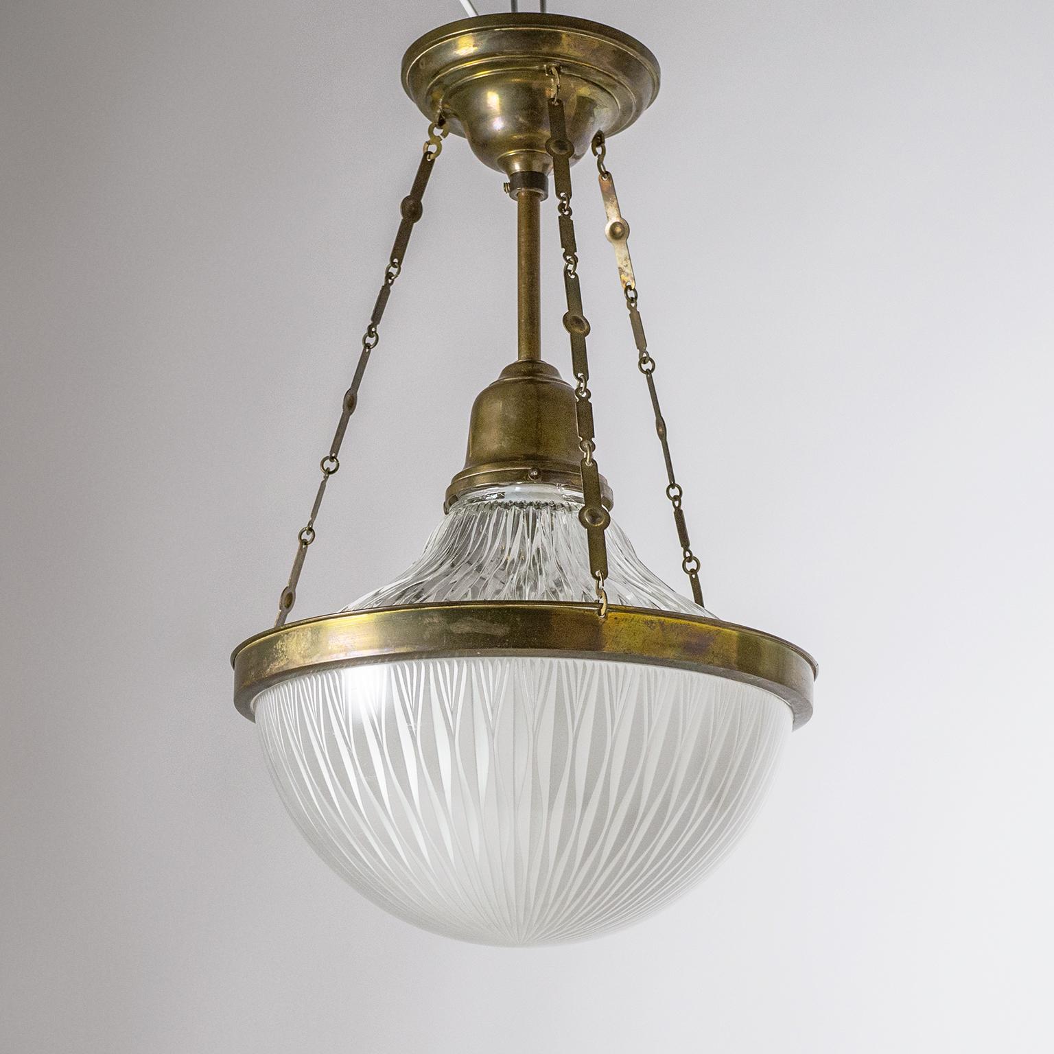 Elegant Art Deco ceiling light in brass and holophane glass, circa 1920. Two holophane glass diffusers are suspended by three sculpted brass chains, the bottom glass has a satin finish on the inside for a soft light dispersion. Good original