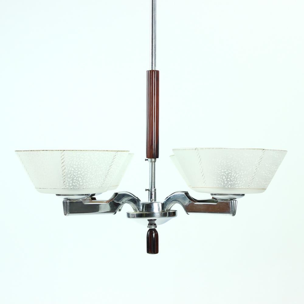 Beautiful ceiling light from Art Deco era in Czechoslovakia. Produced in Czechoslovakia in circa 1940s. The light is on a chrome construction with the typical design of the era. Three arms of the construction hold four glass bowls. Each glass shield