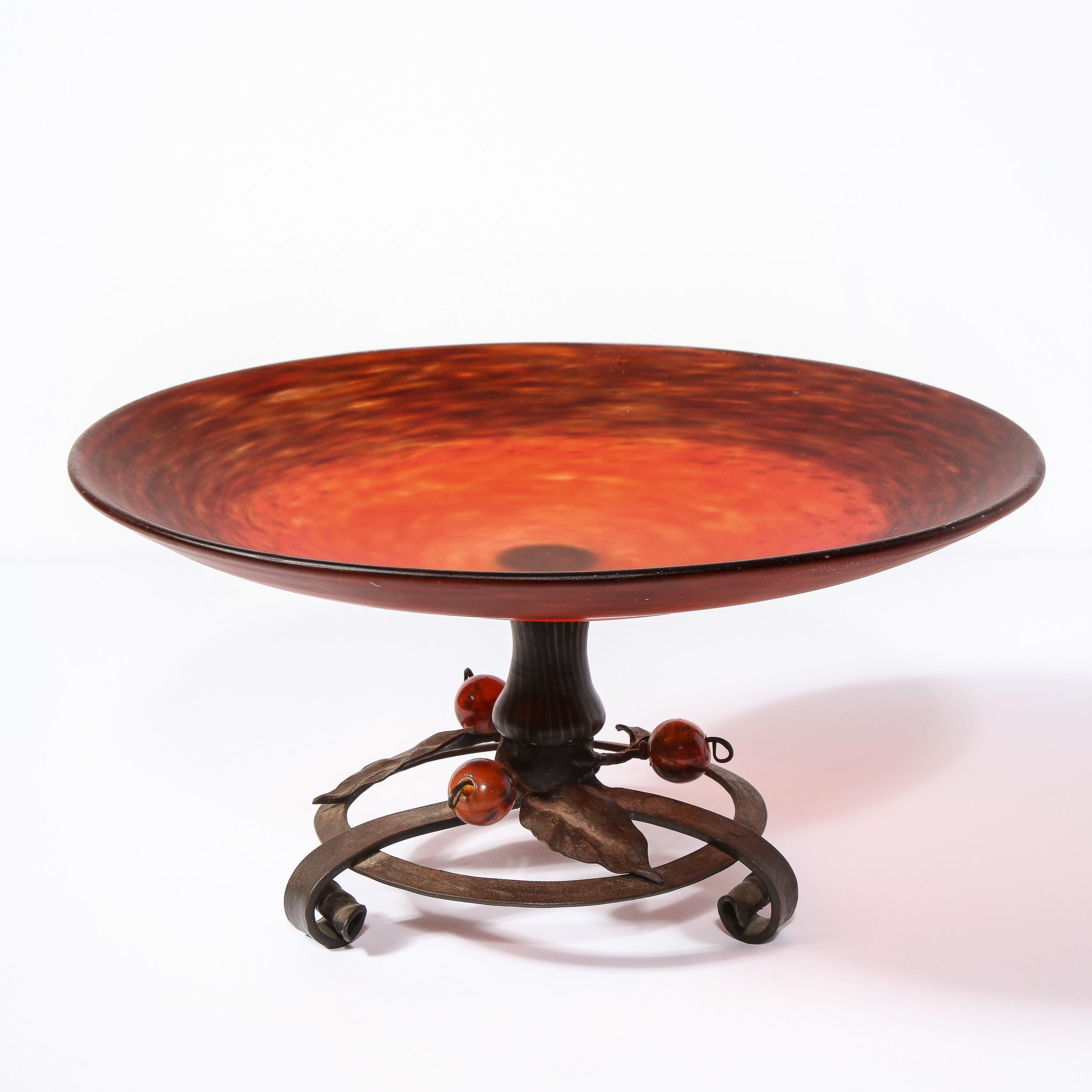 This sophisticated Art Deco centerbowl was realized and signed by Charles Schneider in France circa 1920. It features a mottled carnelian glass top with a wrought iron base adorned with ruby spherical embellishments and stylized foliate detailing.