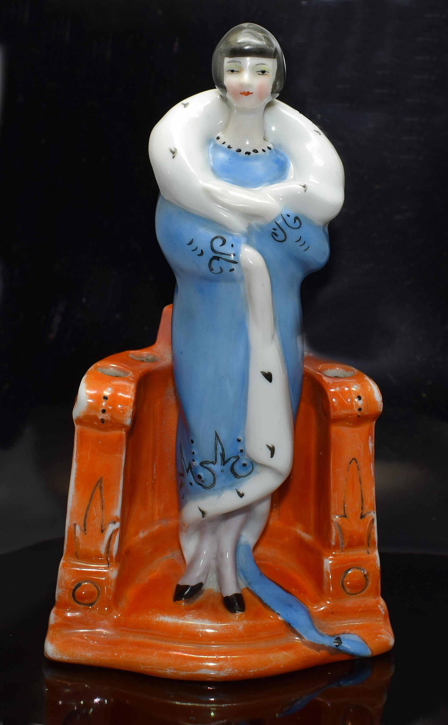 Charming and rare styled Art Deco figural flower frog which is marked to the back with the impressed numerals 6199. This delightful piece features a gorgeous flapper girl with geometric glossy black bobbed hair. She wears a blue dress with black