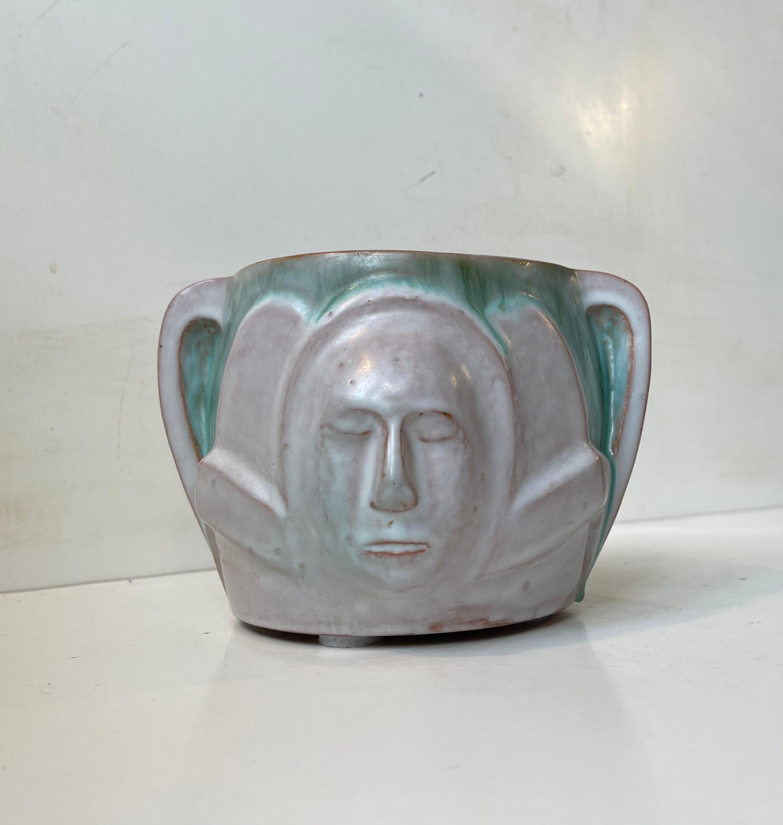Una fioriera o jardiniere unica nel suo genere, realizzata dal ceramista e artista danese Hansen. Realizzato nel suo studio in Danimarca nel 1940-50 circa. Presenta due volti androgini in rilievo, uno per lato. È realizzato con smalti bianchi e