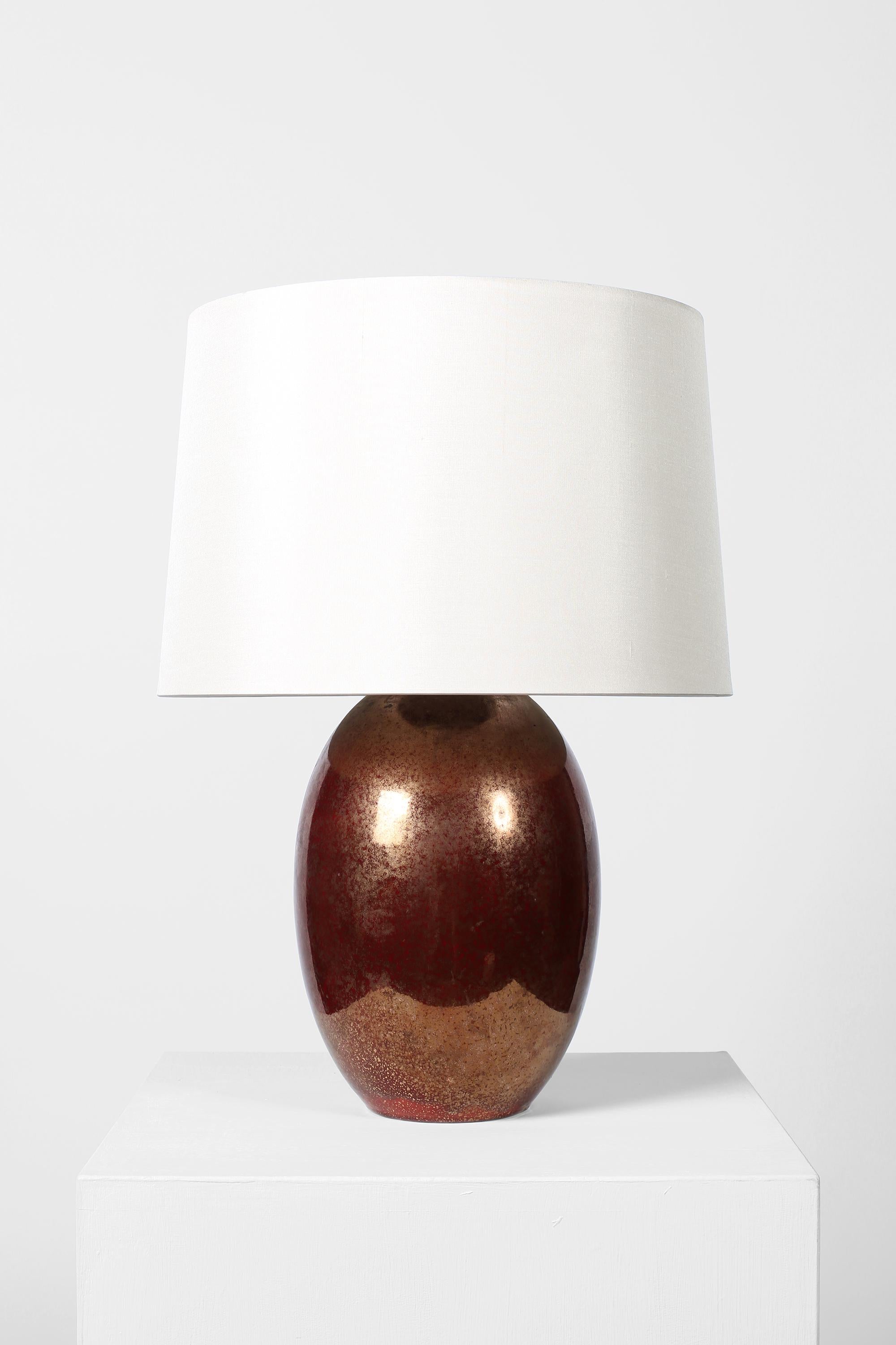 A large Art Deco ovoid ceramic table lamp with deep sanguine and speckled gold metallic glaze, in the manner of Jean Besnard (1889-1958). Indistinctly signed with the monogram JB. French, c. 1930. Supplied with an off-white dupion silk