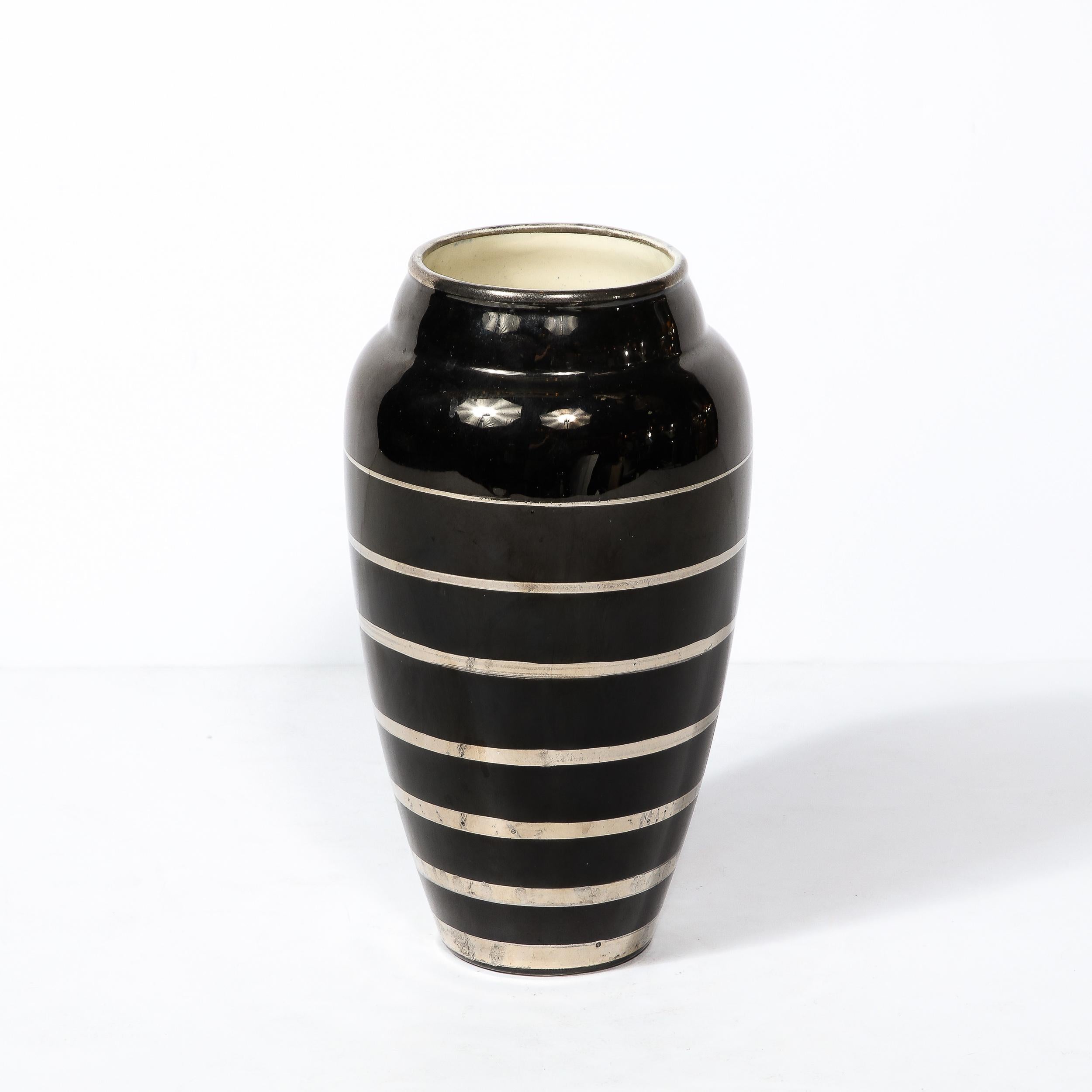 This Art Deco vase is an exceptional example of this iconic style, with a timeless form and beautiful glazed surface and originates from the Belgium Circa 1935. Glazed in a beautiful ivory black with horizontal banded detailing in a reflective