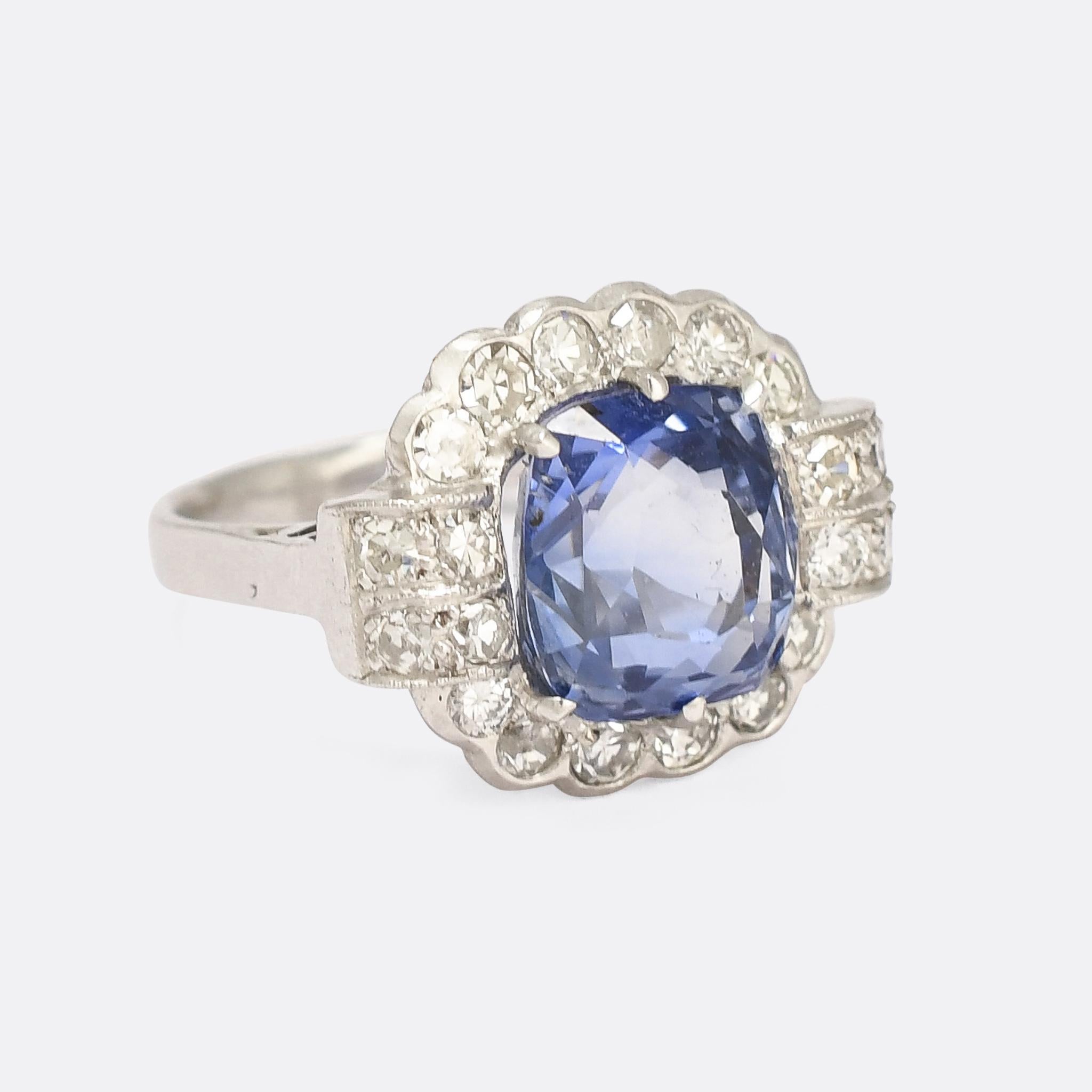 A stunning Art Deco period flower cluster ring crafted in France in the 1920s. The quality of the stone reflects the quality of the mount; a beautiful Ceylon sapphire displaying a vibrant blue at the paler end of cornflower. The cushion cut stone is