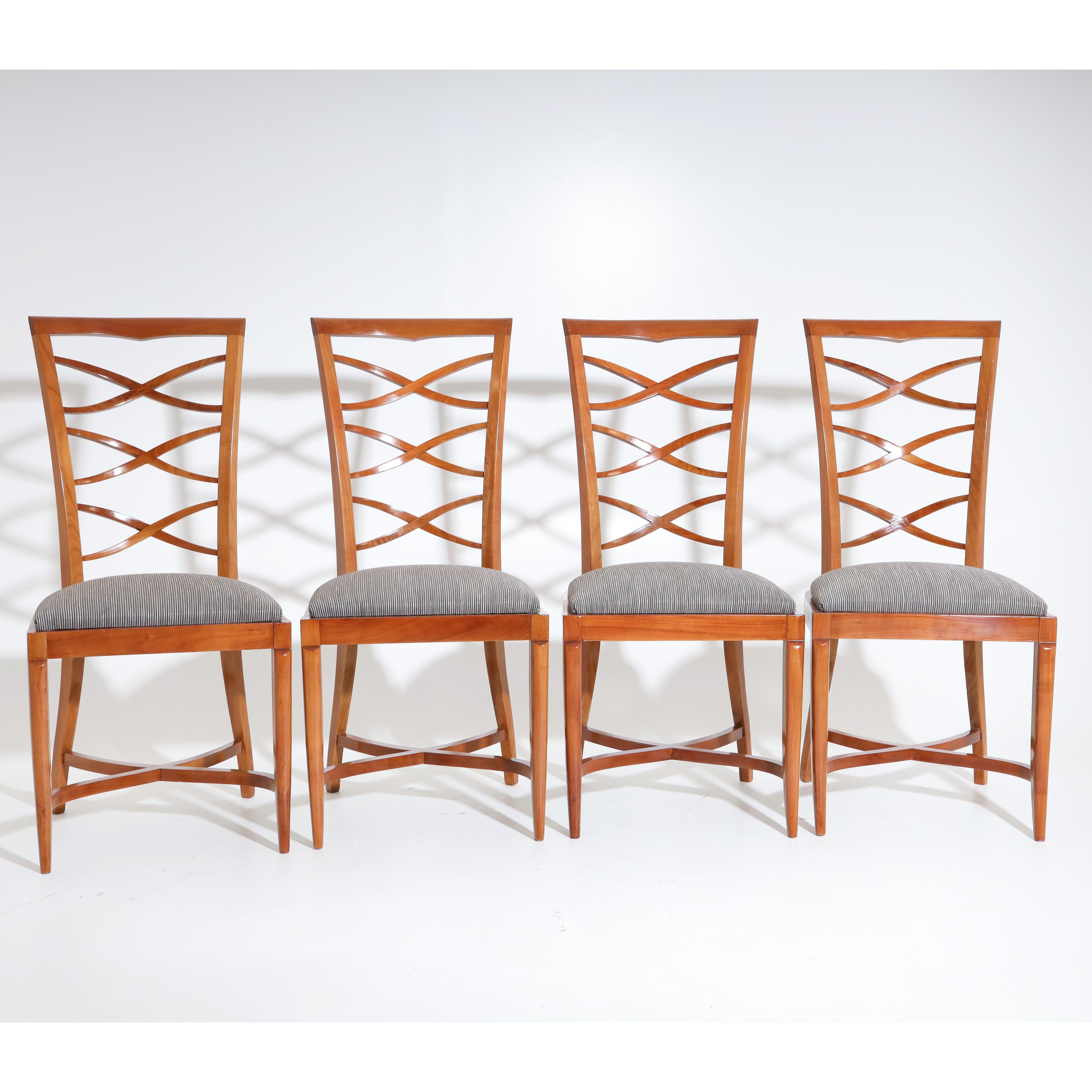 Set of four Art Deco chairs in cherry, with trapezoidal openwork backrests and upholstered seats. The chairs stand on elegantly curved legs with X-shaped bracing. The chairs are newly covered with a silver-grey striped fabric and hand polished.