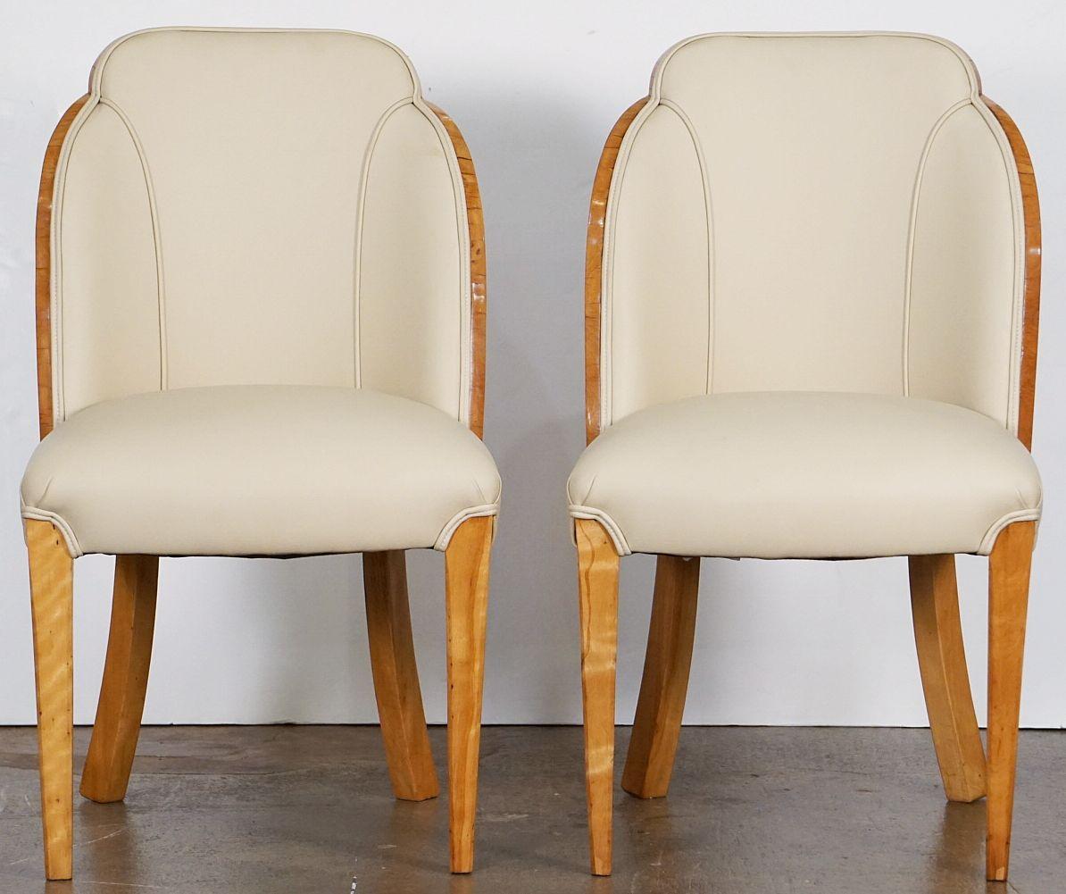 A pair of comfortable English cloud-backed tub chair from the Art Deco period - each chair featuring a bleached burr walnut wraparound veneer, re-upholstered back and seat in cream leather, on tapering chamfered legs. Attributed to Harry & Lou