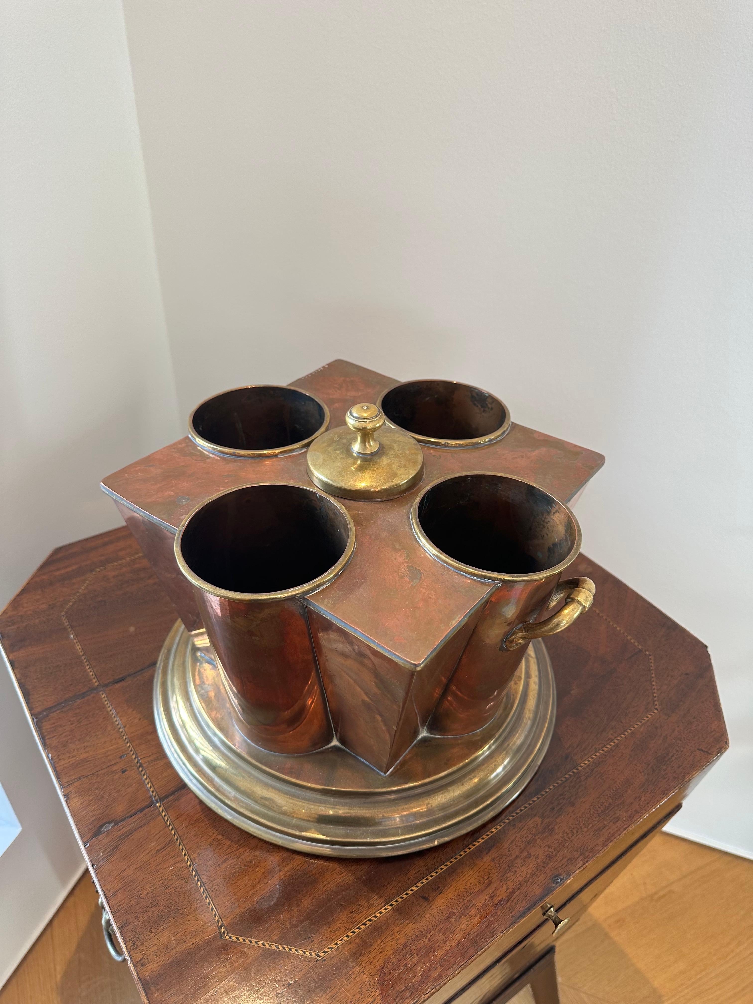 An Art Deco Style champagne cooler by G.Peak & Co, London. The tapering sides with four bottle apertures centered by an ice compartment with detachable cover, on stepped circular base, made of brass and copper.

