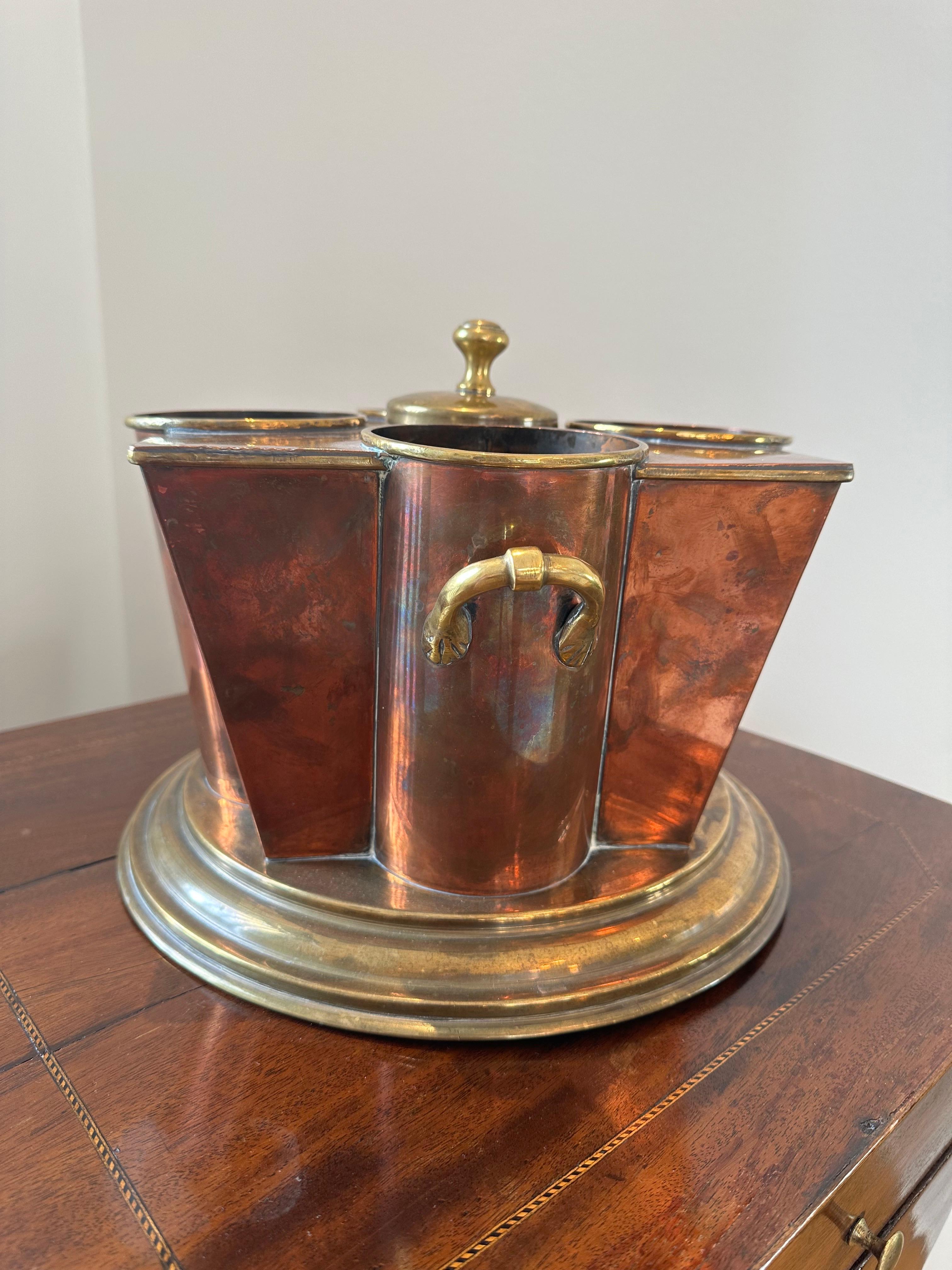 An Art Deco Style champagne cooler by G.Peak & Co, London. The tapering sides with four bottle apertures centered by an ice compartment with detachable cover, on stepped circular base, made of brass and copper.

