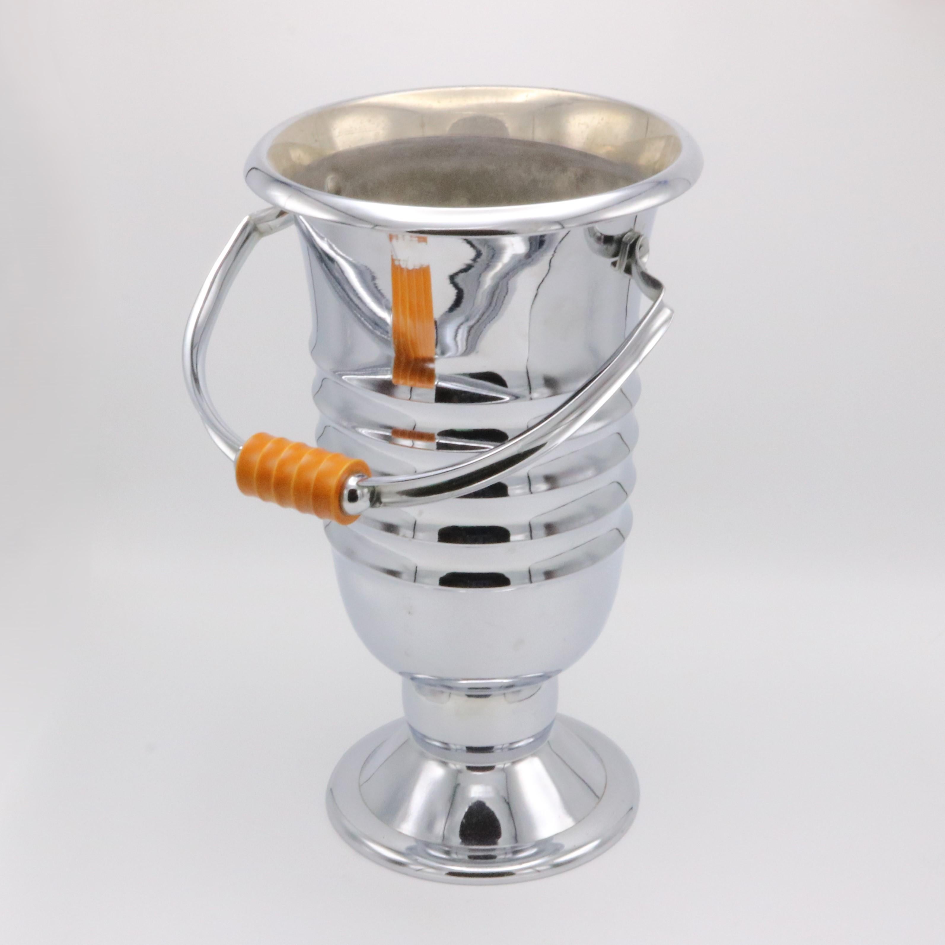Una champañera de época Art Déco procedente de Francia hacia 1930. El elegante cubo para vino es de latón niquelado con asa de baquelita. El alto cuerpo está adornado con una serie de anillos concéntricos y se alza sobre un pie elevado.