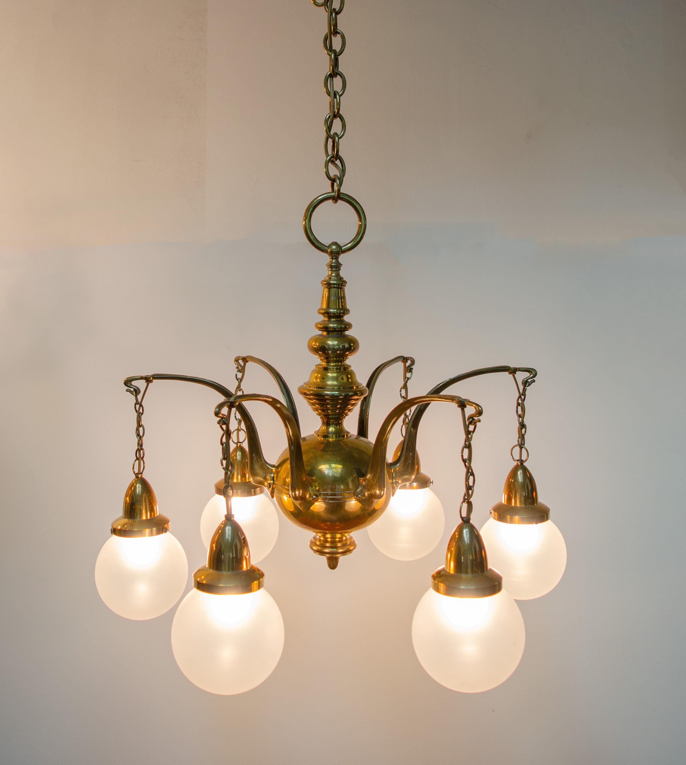 This six-arm Art Deco ceiling chandelier made of brass dates from around 1930. The six arms have lampshades made of opal matt spherical glass. The brass chain can be shortened if the room height requires it. The classic, elegant chandelier can be