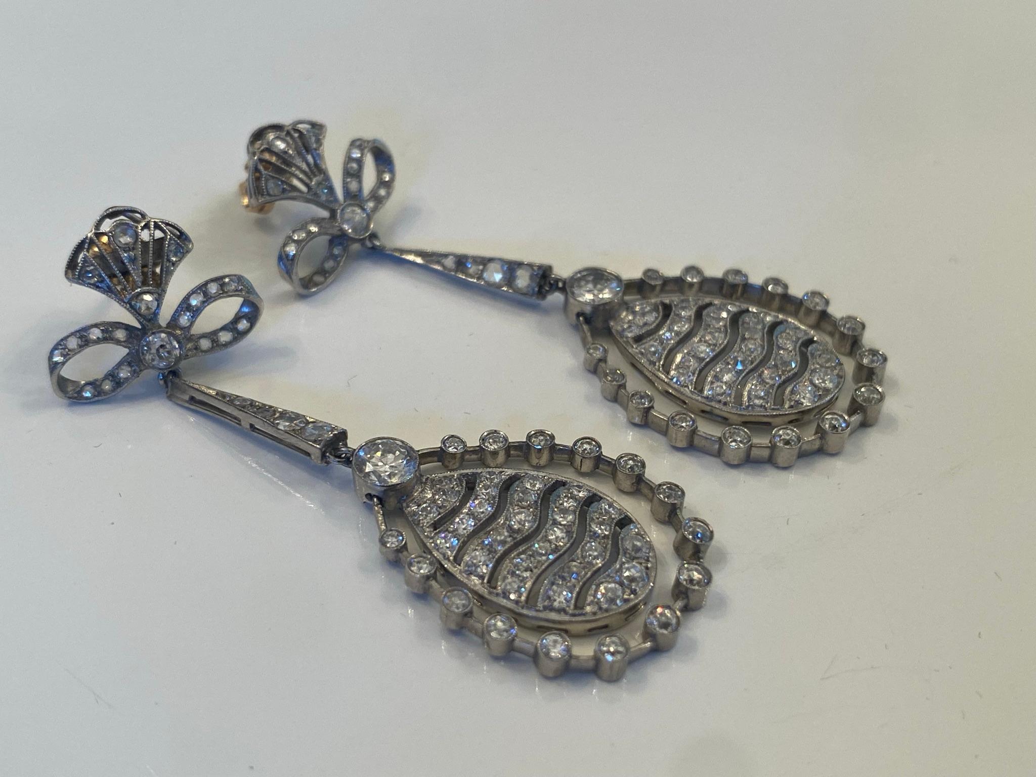 Crafted in the 1920s from platinum, these stunning Art Deco chandelier earrings feature approximately 2.75 carats of Old European cut and rose cut diamonds arrayed over a dangling and fanciful design of bows and ovals and halos. The earrings measure