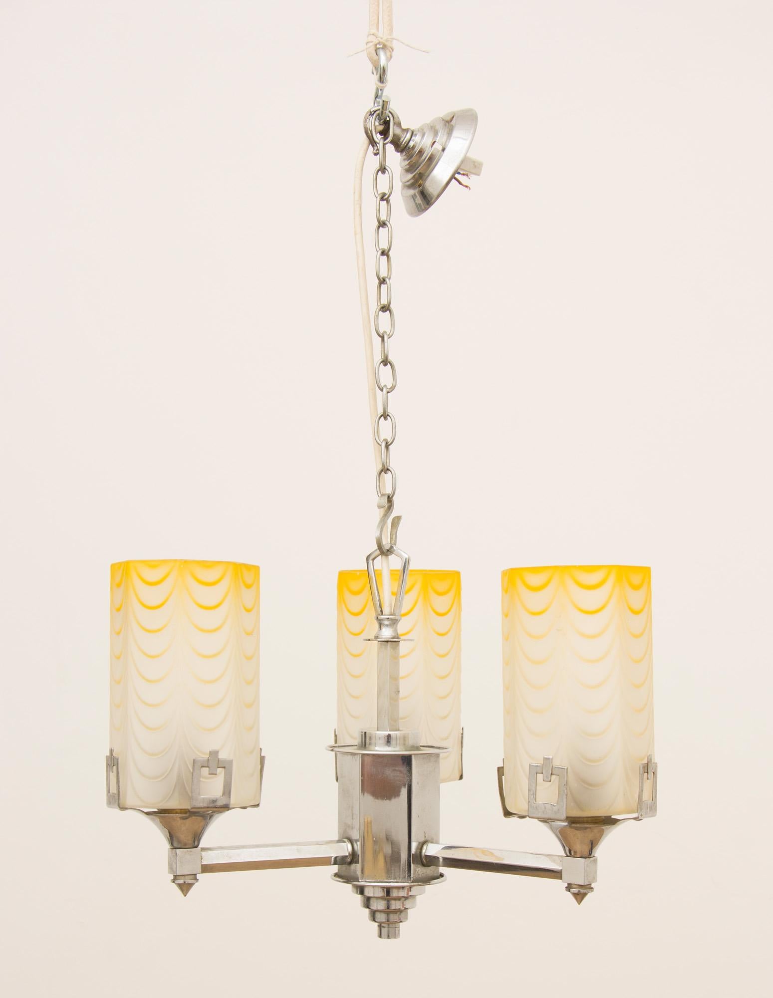 Art Deco ceiling light.
Art Deco three branch chandeliers with original yellow swaged glass cylinders, nice stepped chrome base to the column, the shades are held in place with three squared chrome clips.
The drop can be adjusted with