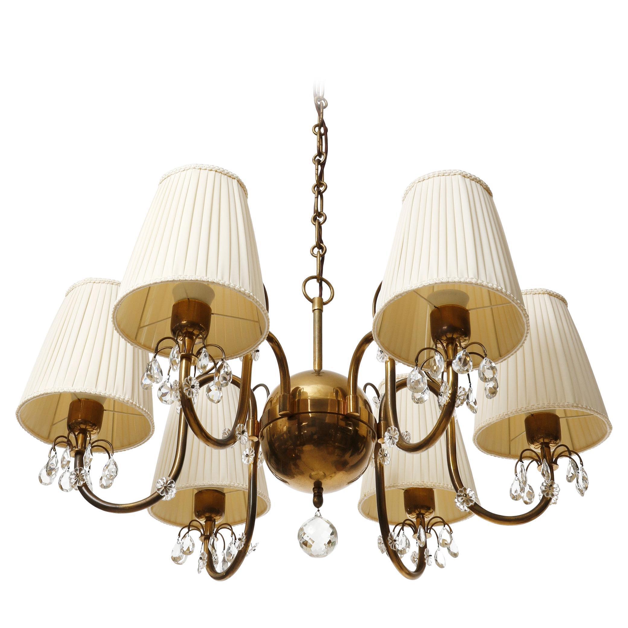 Magnifique lustre à six branches en laiton et abat-jour en tissu plissé de couleur crème, fabriqué en Autriche dans les années 1930.
Les bras aux courbes organiques sont décorés de pièces en verre taillé. Les pièces en laiton présentent une belle