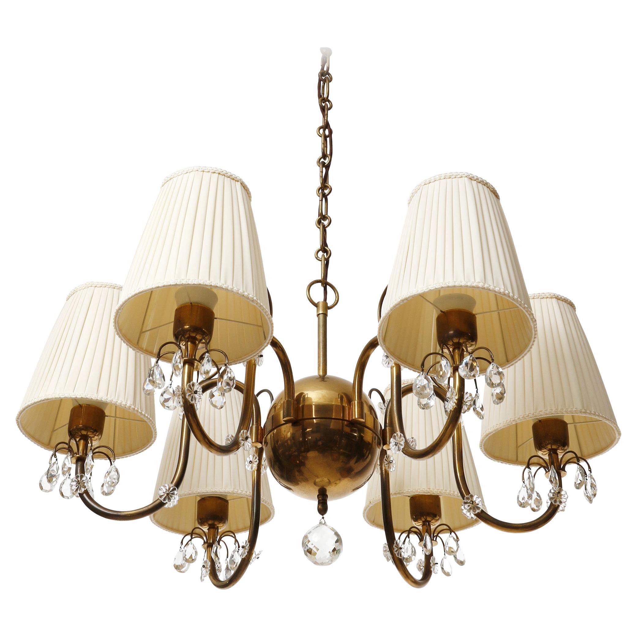 A large and fantastic six-arm pendant chandelier made of brass and cream colored pleated fabric shades, manufactured in Austria in 1930s.
The organically curved arms are decorated with cut glass pieces. The brass parts have lovely patina and a warm