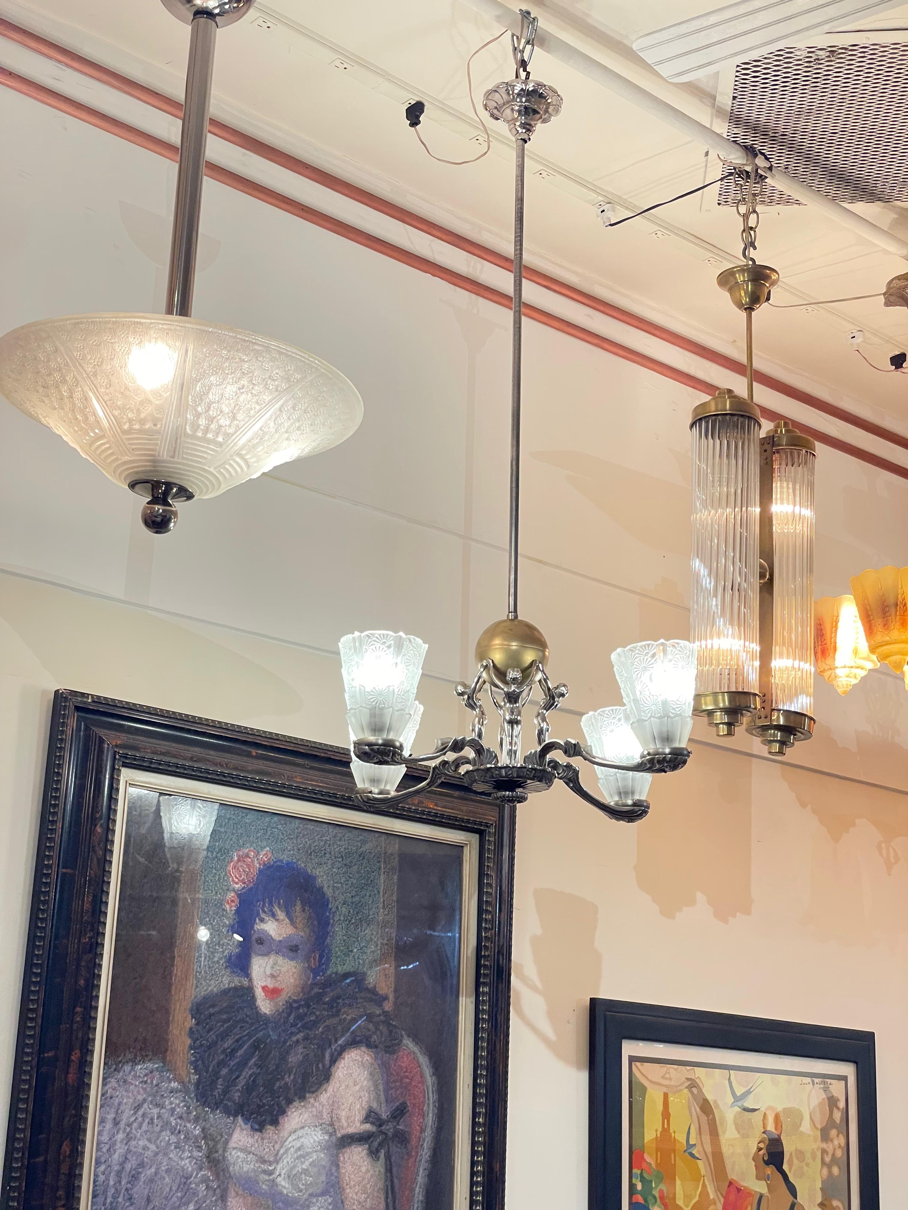 An Art Deco Chandelier with four silvered sculptural female nudes holding up a golden ball as the centerpiece. Four French pressed floral frosted glass shades and unusual metalwork throughout make this a truly unique lighting fixture. The women