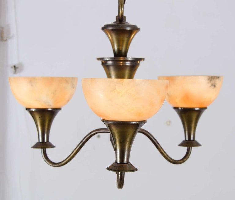 The three arms hold alabaster uplighter shades. Brass metal frame is patinated in bronze. Chandelier is classical in form and shape made in the 1930'-40s, France.