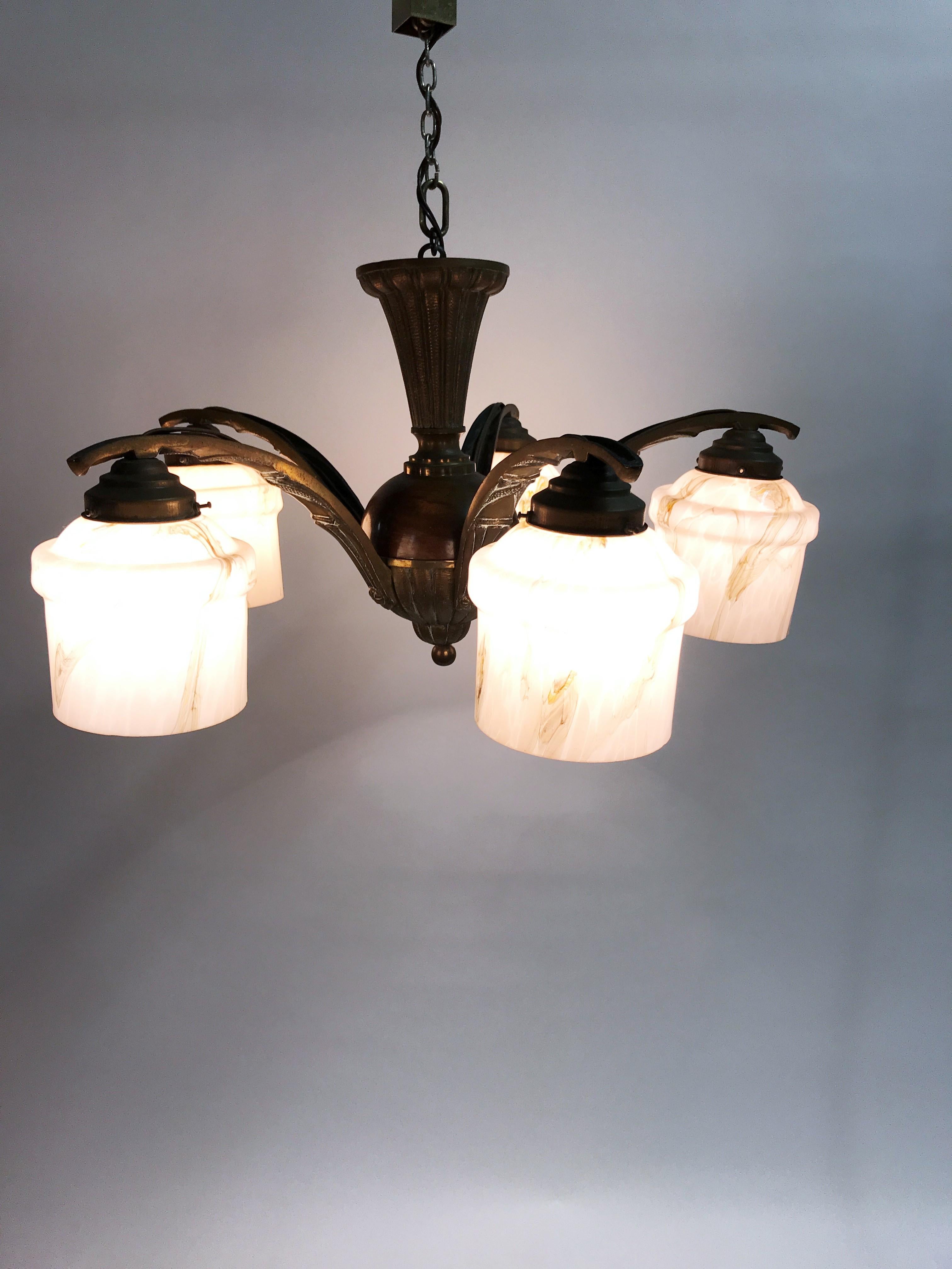 Art deco era chandelier with pink marbled glass shades.

This 5 lightpoint chandelier is made bronze and wood.

The marbled shades give a wonderful light effect.

Good original condition.

Tested and ready for use with regular E27 light