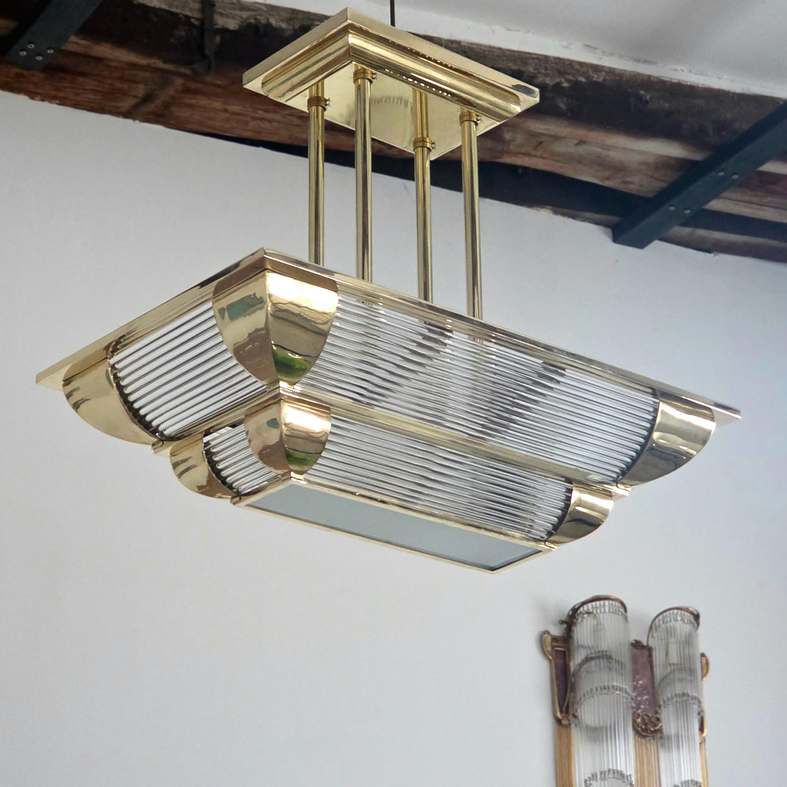 Art Deco chandelier in polished bronze, with geometric lines and glass diffusers, combining the elegance and symmetry typical of the 1930s.