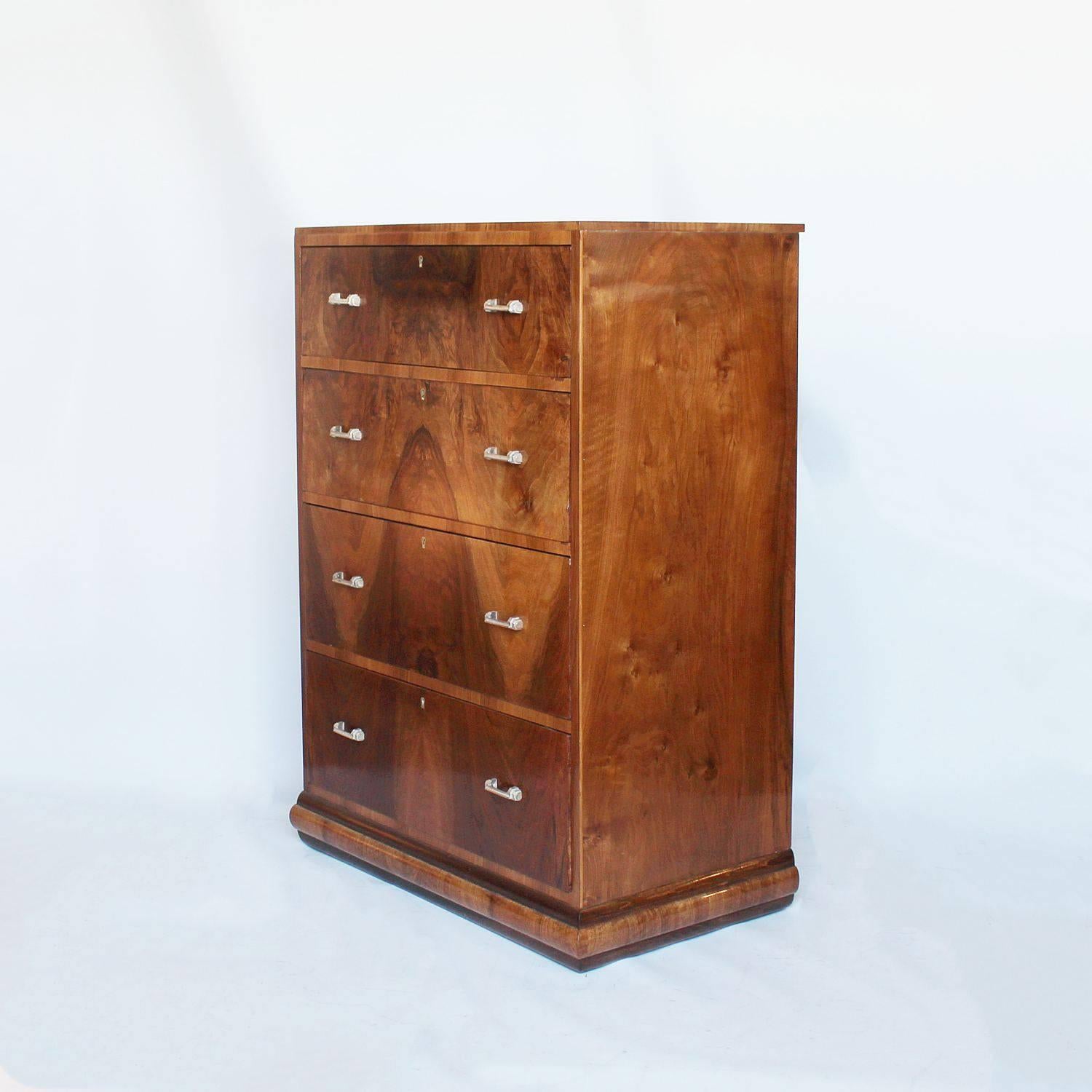 An Art Deco chest of four drawers of augmenting height with original metal handles and panelled back. Figured walnut set over a straight grain walnut base.

 
