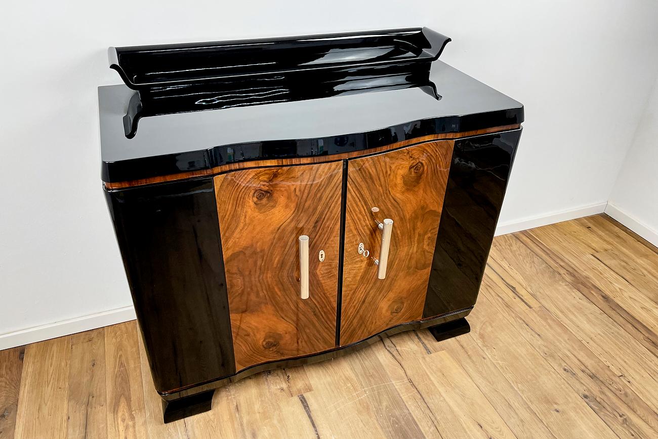 Art Deco chest of drawers from Germany around 1930 in black high gloss and walnut. We got this chest of drawers from Berlin, where it was built around 1930. The fittings were added by us. The entire piece of furniture is provided with a multi-layer