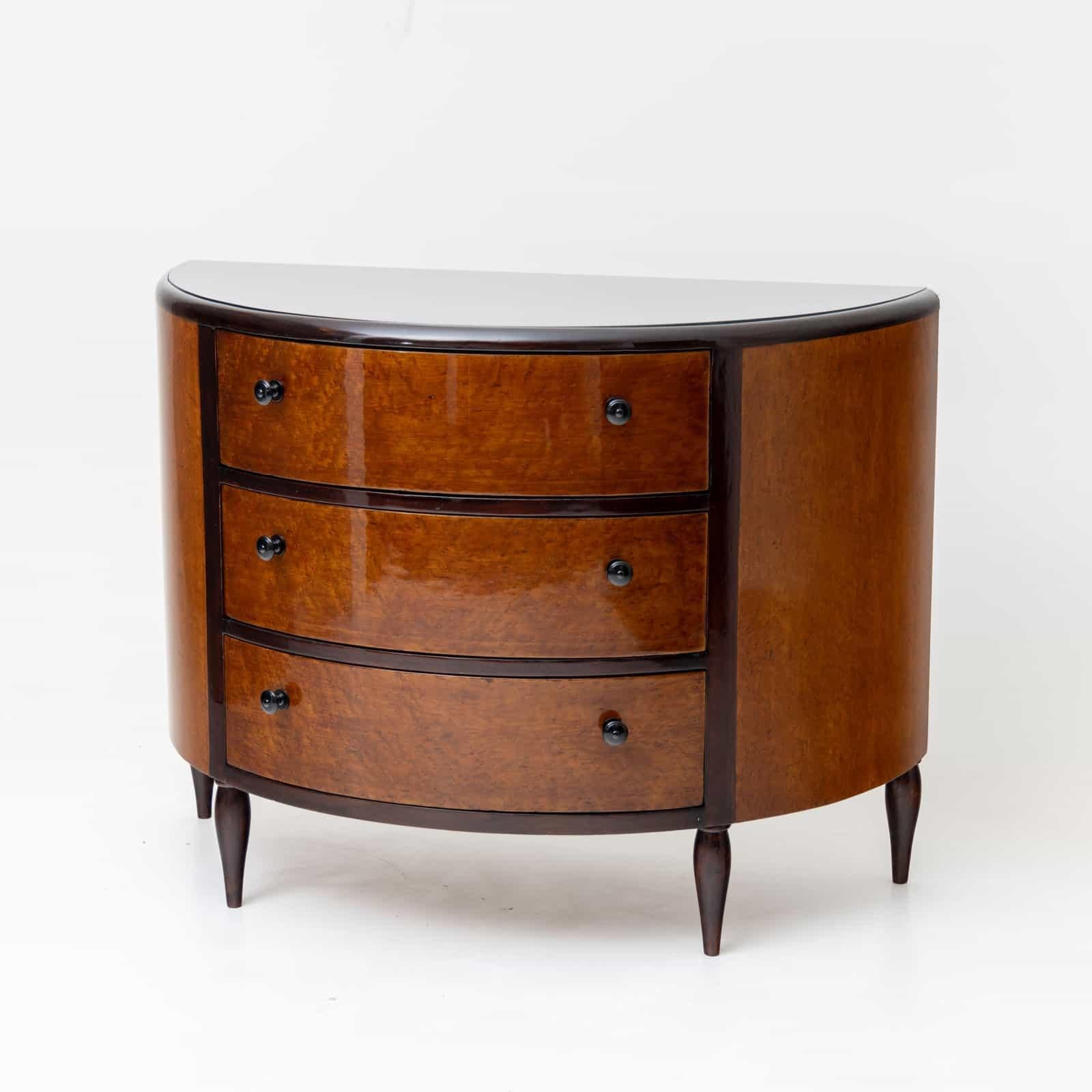 Art Deco chest of drawers in demi-lune shape with three drawers and inlaid glass top. The chest of drawers stands on conical feet and is veneered in thuja root.