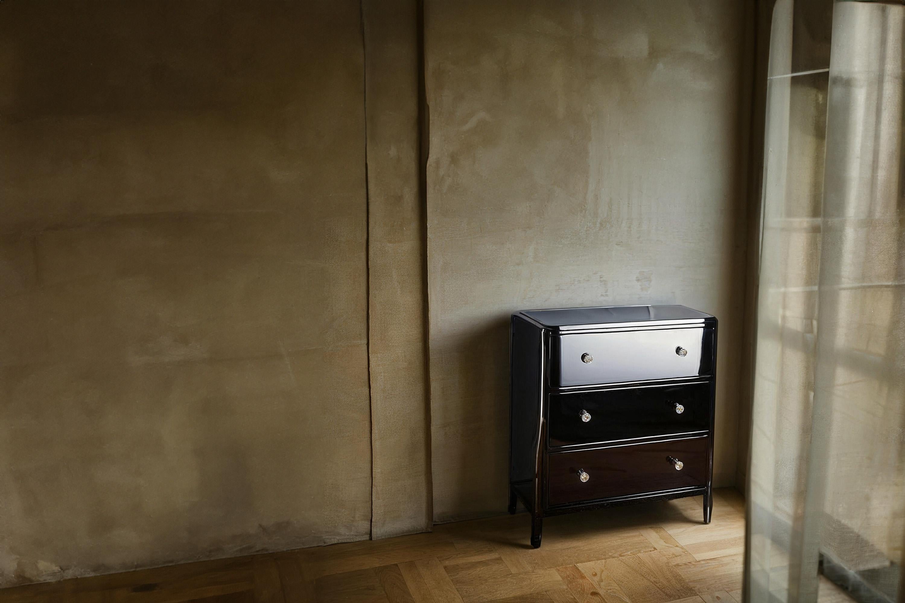 Preciosa cajonera pequeña con laca de piano muy elegante y tiradores cromados. La cómoda tiene tres cajones y está equipada con tiradores redondos cromados. La superficie se ha sellado con un barniz de alto brillo. La superficie negra ha sido