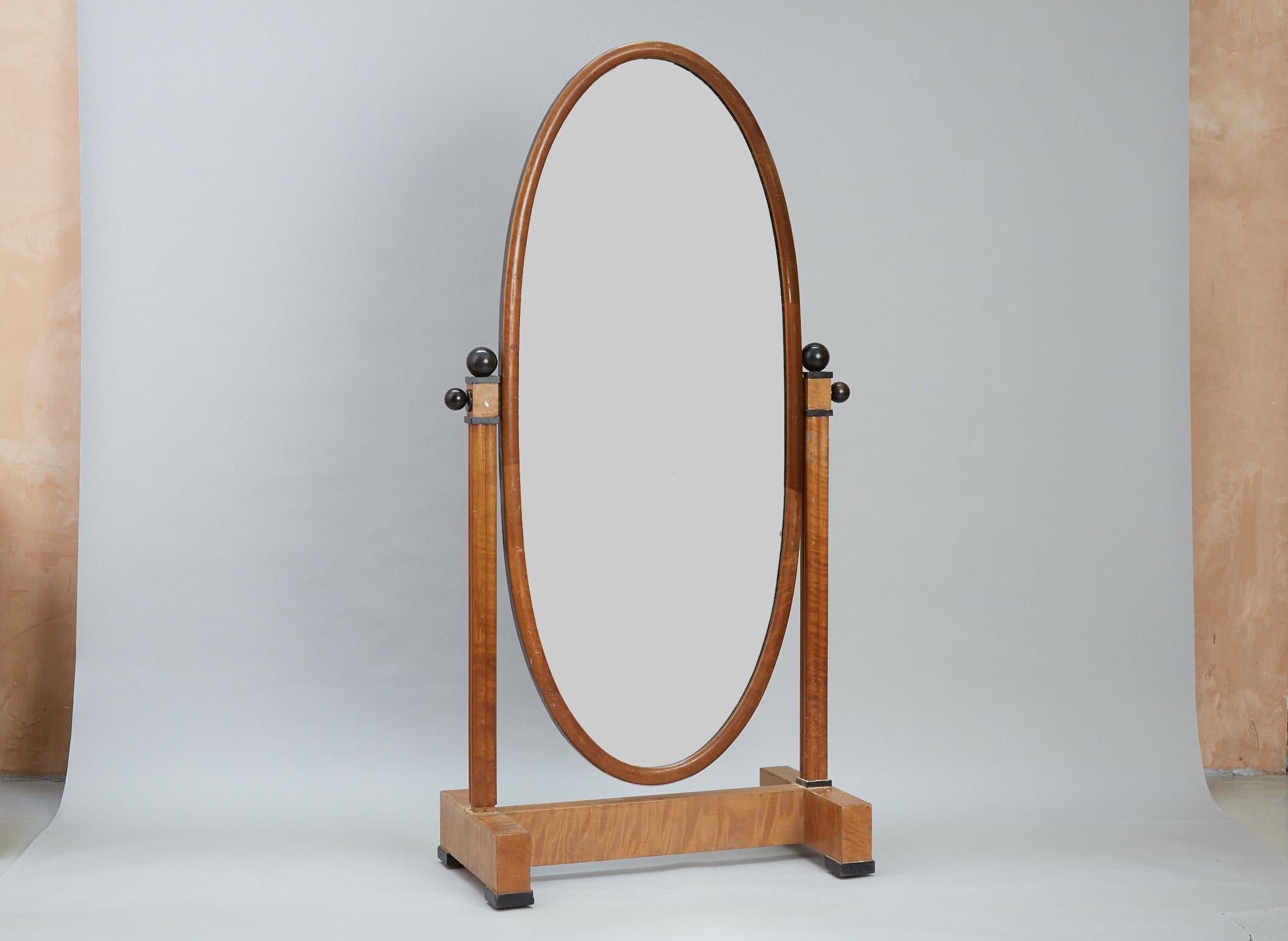 A fabulous Art deco cheval floor mirror. 
Some losses to the trim but still a very stylish piece.

The large oval mirror can be adjusted in both directions and is hung from two large fasteners on each side of the stand. 

The mirror is adorned with