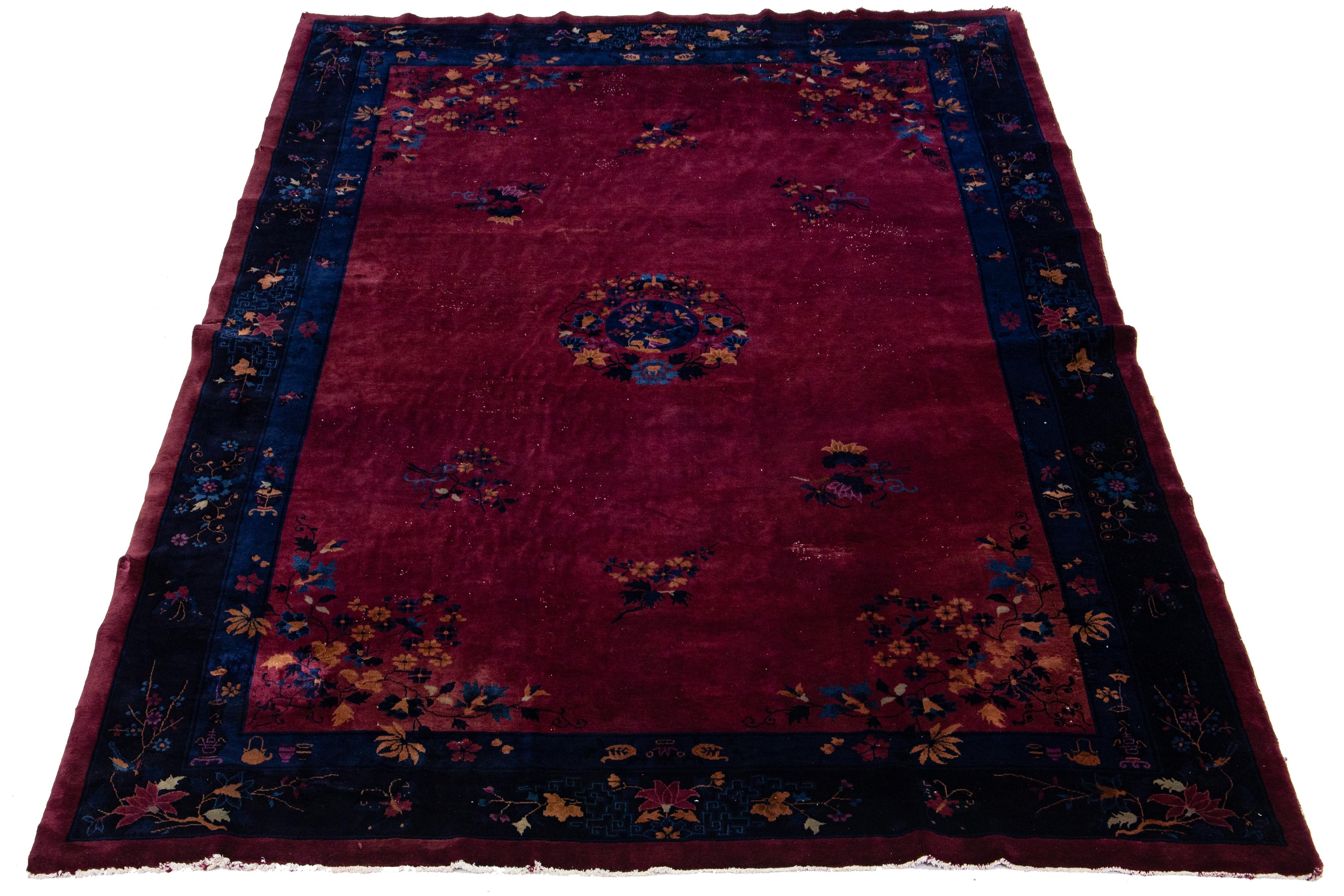 This antique Chinese Art Deco rug is hand-knotted with wool and features a burgundy red field with a navy blue multicolor floral design. The classic Chinese floral pattern is elegant and sophisticated.

This rug measures 9'11