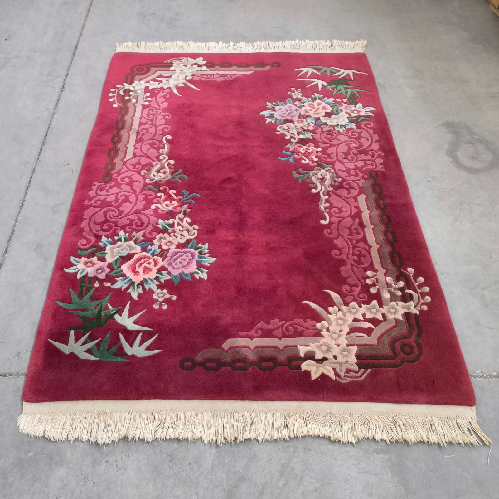 Tapis chinois en laine Vintage Art of Vintage, années 1930.
Il s'agit d'un tapis tissé à la main en poils de laine sur chaîne de coton, avec de riches motifs de fleurs et de bambous, sur un fond framboise foncé. Des motifs d'angle en forme de chaîne